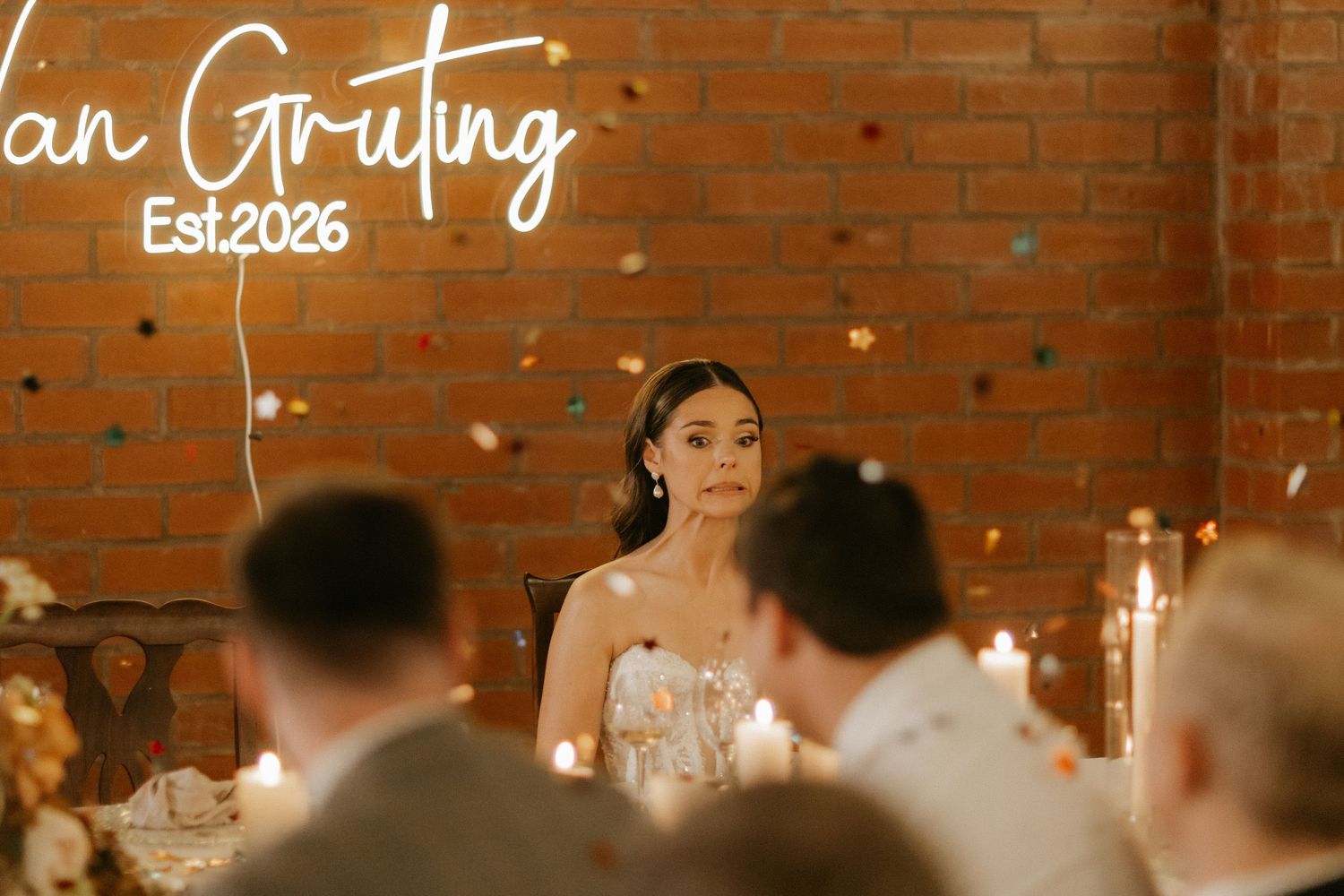 Bride sits at wedding reception head table beneath Van Gruting Est.2026 neon sign.