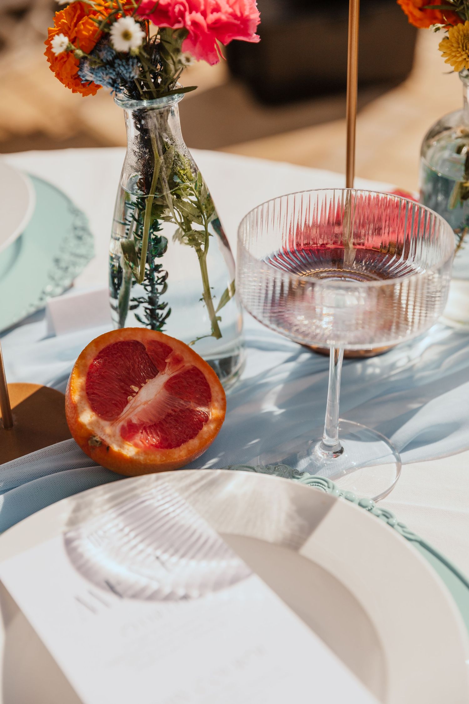Elegant table setting with flowers in vase, wine glass, and sliced grapefruit in natural light.