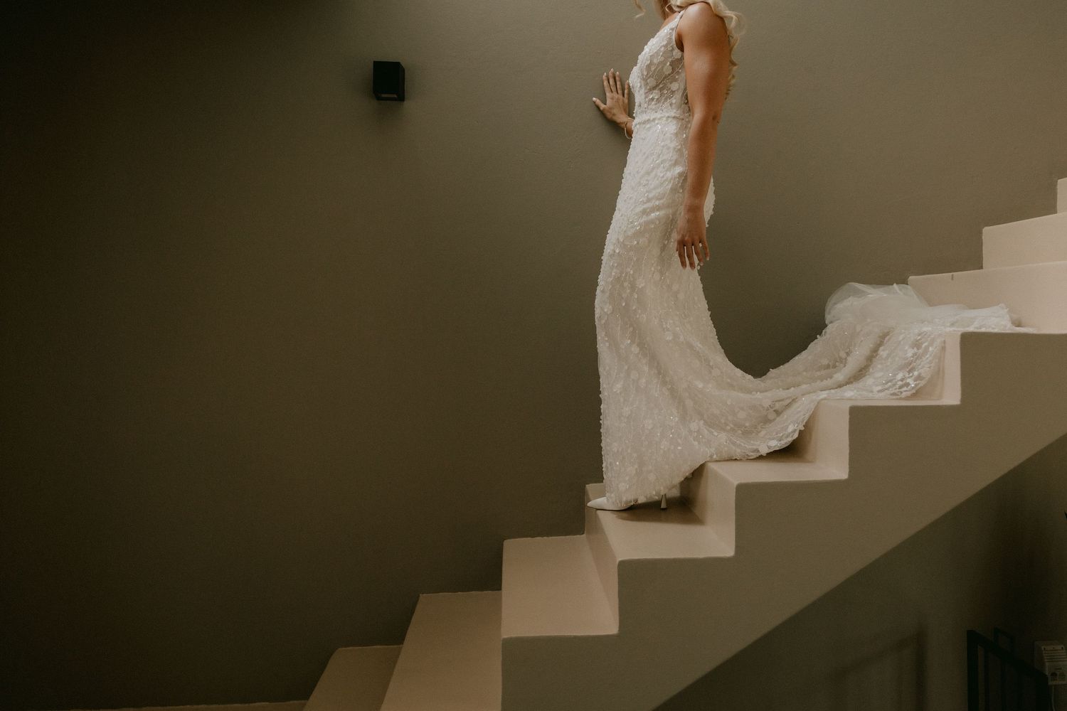 Wedding dress detail shots showing flowing white gown on staircase in moody lighting.