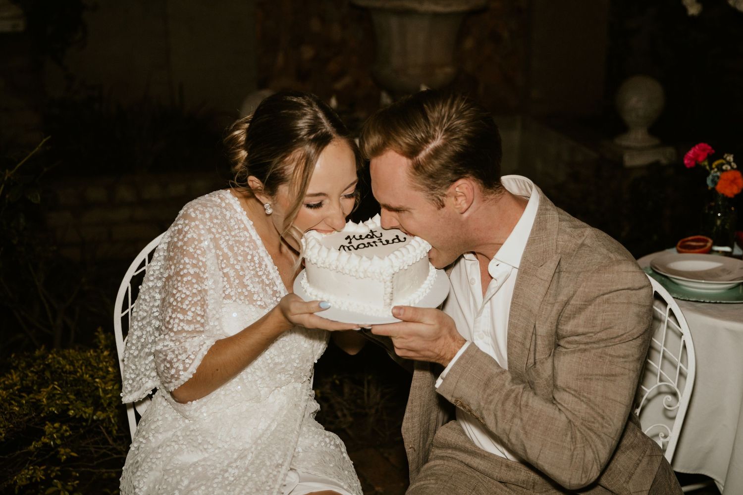 Playful wedding couple laughing while sharing cake at their reception.