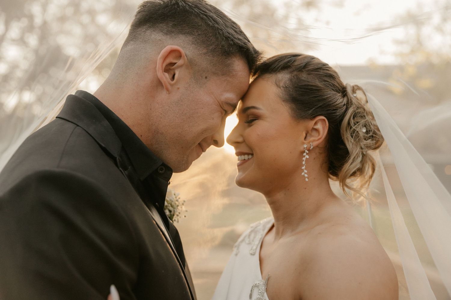 A romantic wedding couple shares an intimate moment at sunset with their foreheads touching.