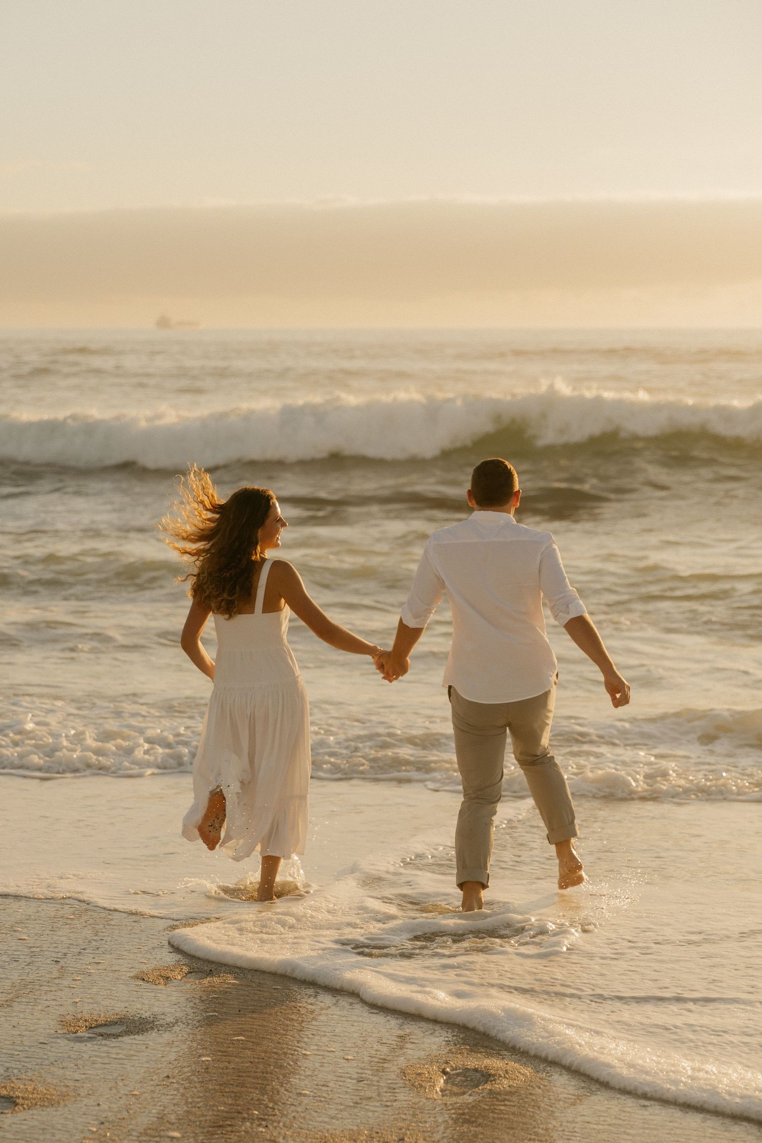 A couple walks hand in hand through the surf during sunset on a scenic beach.