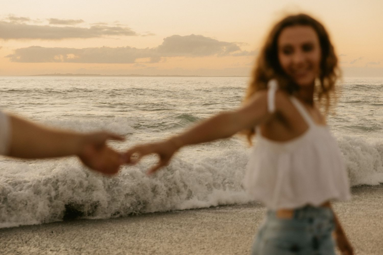 A dreamy sunset beach scene with someone reaching out while waves crash behind.