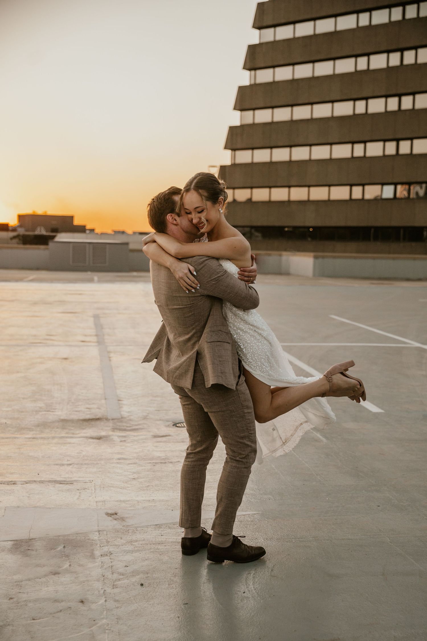Couple sharing intimate dance on rooftop during sunset with urban architecture backdrop.