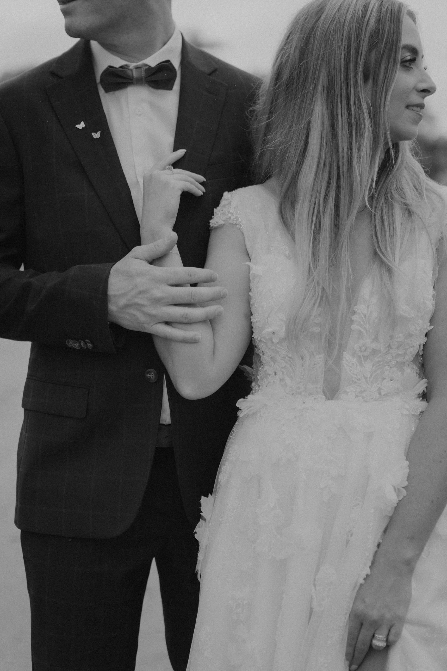 A black and white wedding photo series showing close-up details of a bride in a lace dress with her groom in a tuxedo.