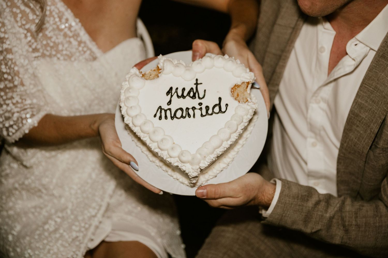 Heart-shaped white wedding cake with 'just married' text held in hands.