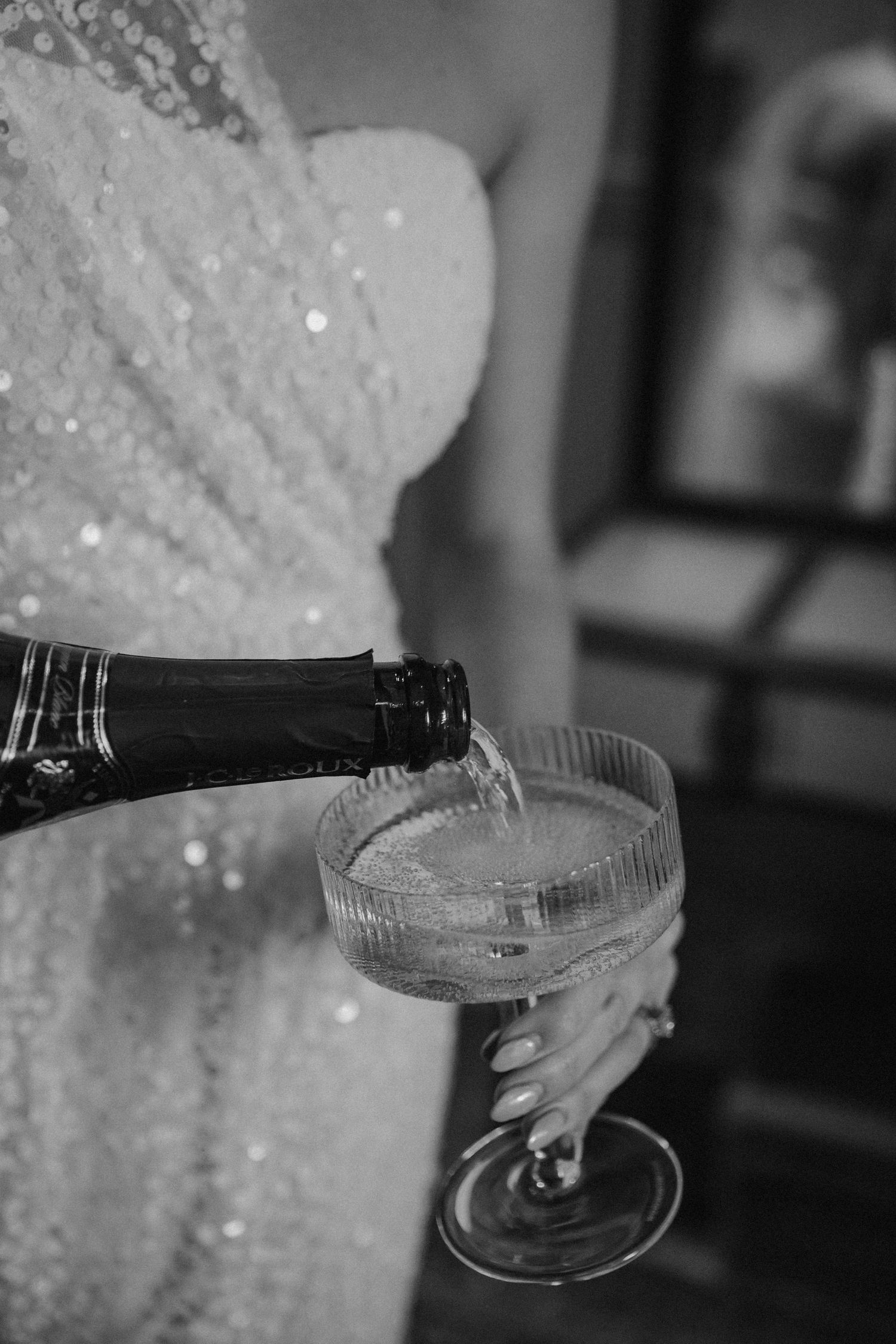 Champagne being poured into a vintage coupe glass, with a sparkly wedding dress in view.