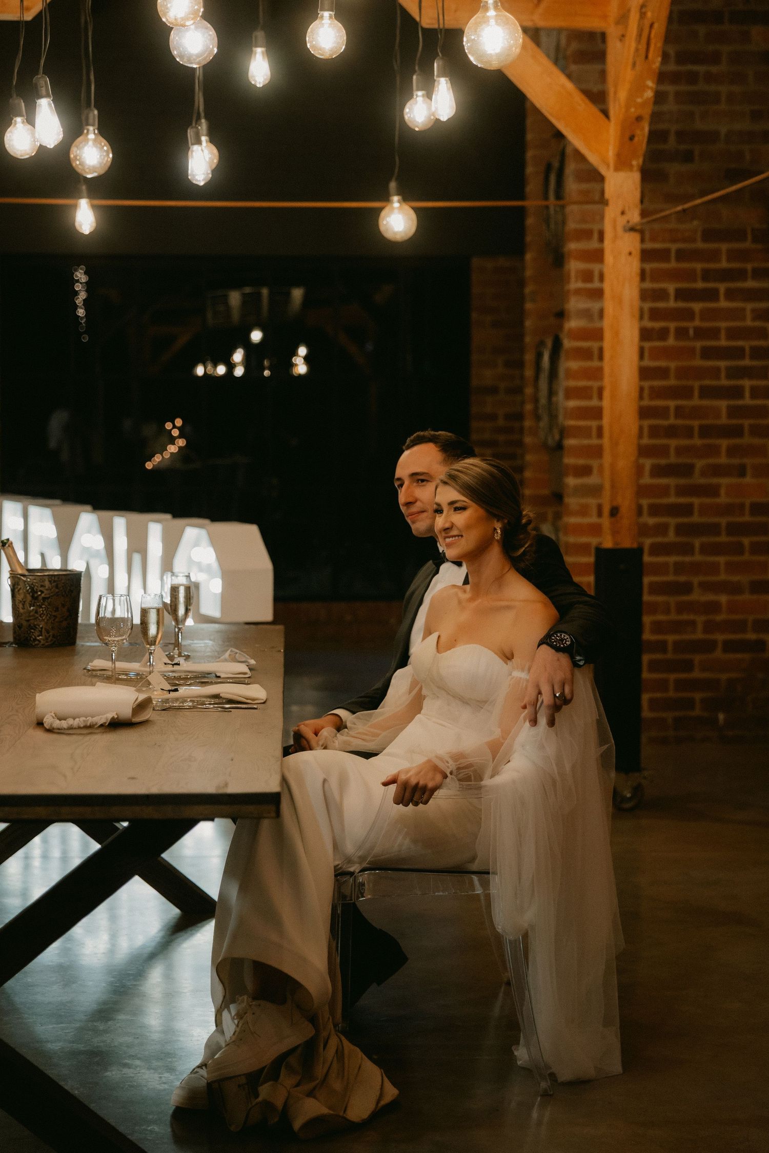 A romantic candlelit wedding reception venue with hanging Edison bulbs illuminating a rustic brick interior.