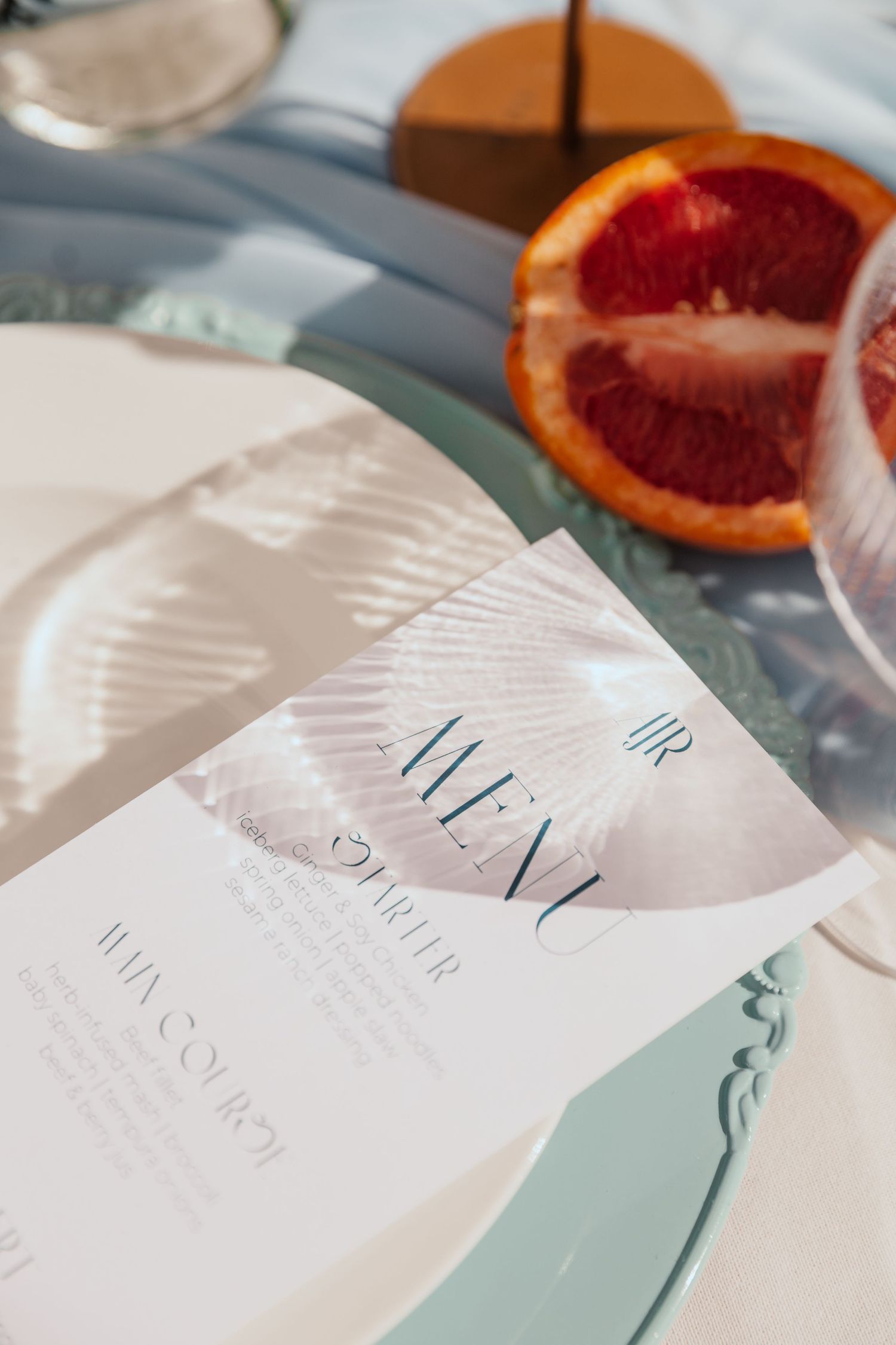Wedding menu card on mint-colored charger plate with citrus fruit decor.