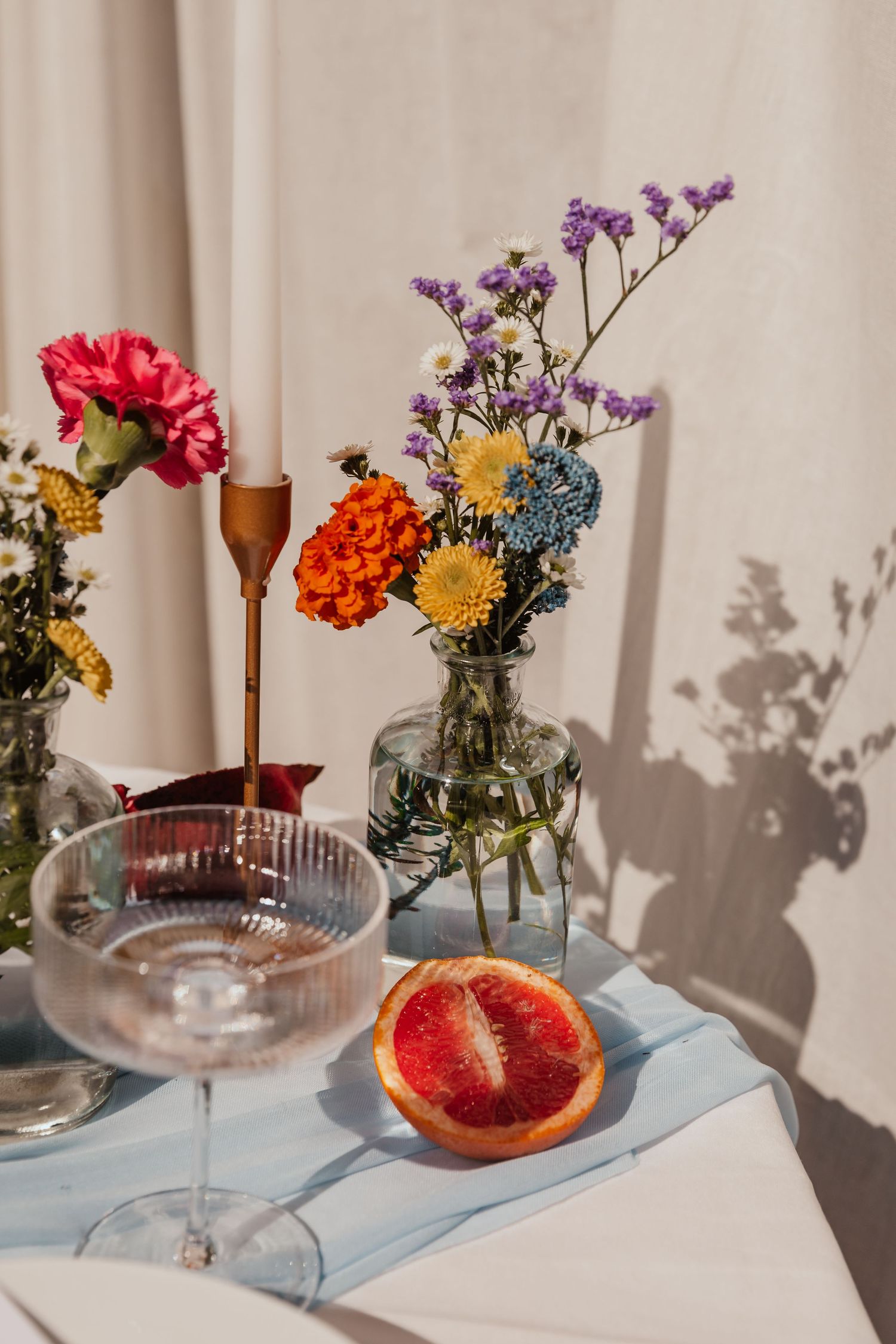 Colorful wildflower arrangement with grapefruit slice and wine glasses on white tablecloth.