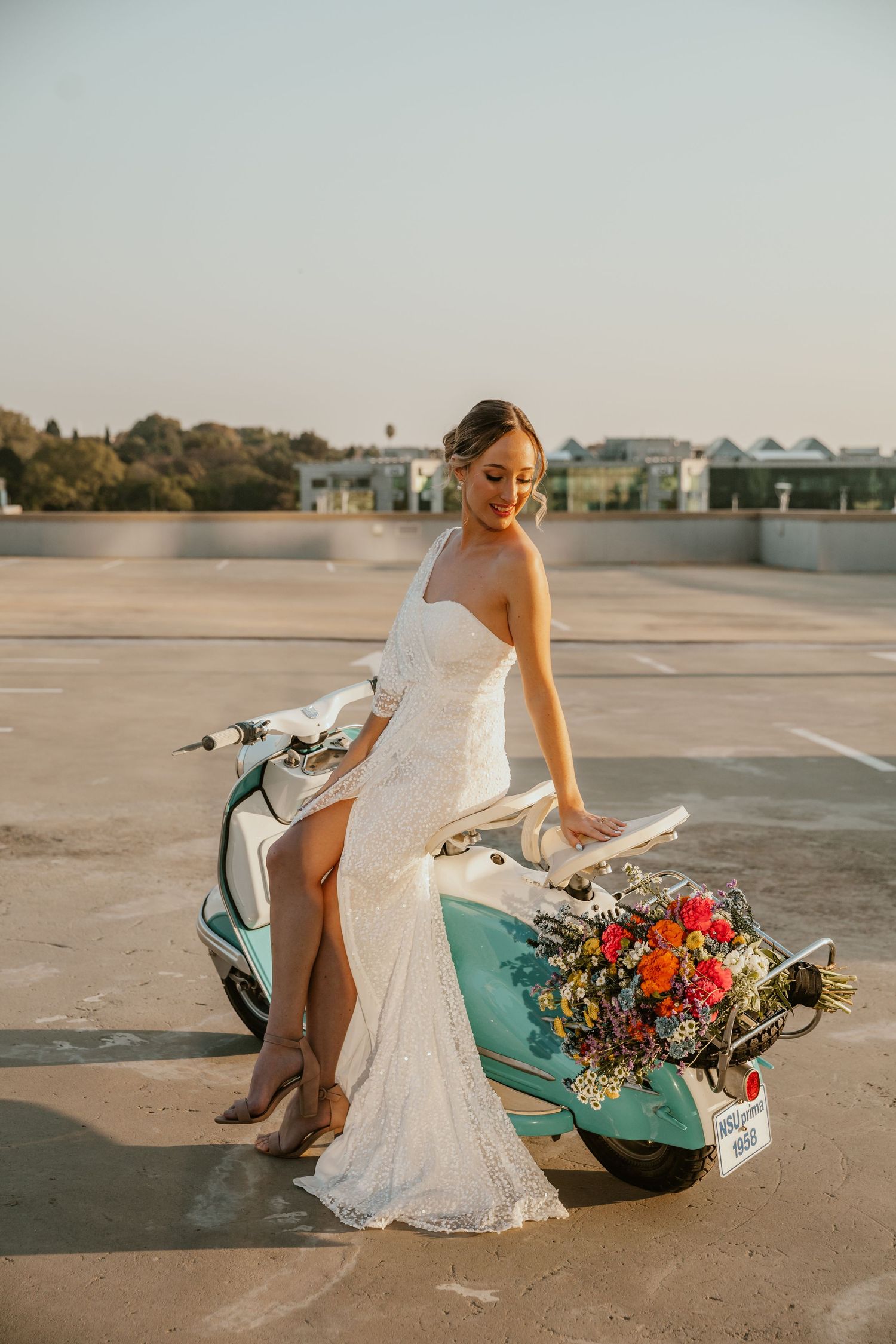 Bride in lace wedding dress posing with vintage turquoise scooter and colorful bouquet.