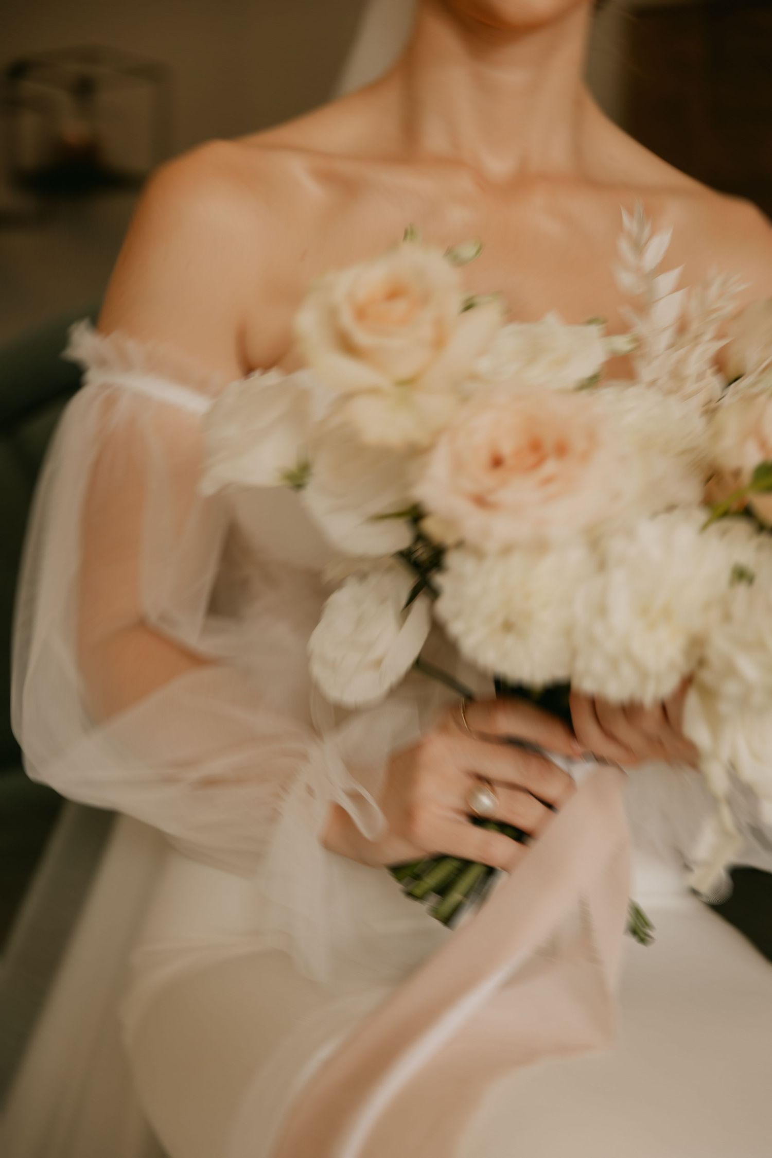 A delicate bridal bouquet of blush and white peonies with soft tulle fabric draping in the background.