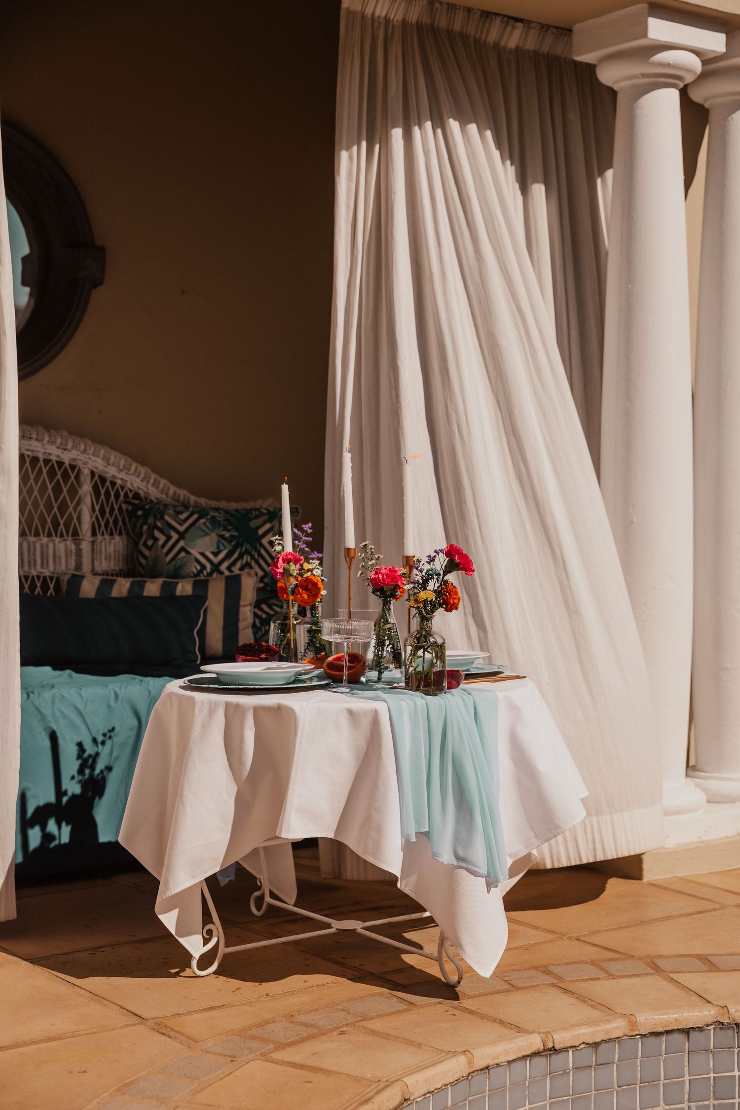 Intimate outdoor dining setup with white tablecloth and floral centerpieces near white pillars.