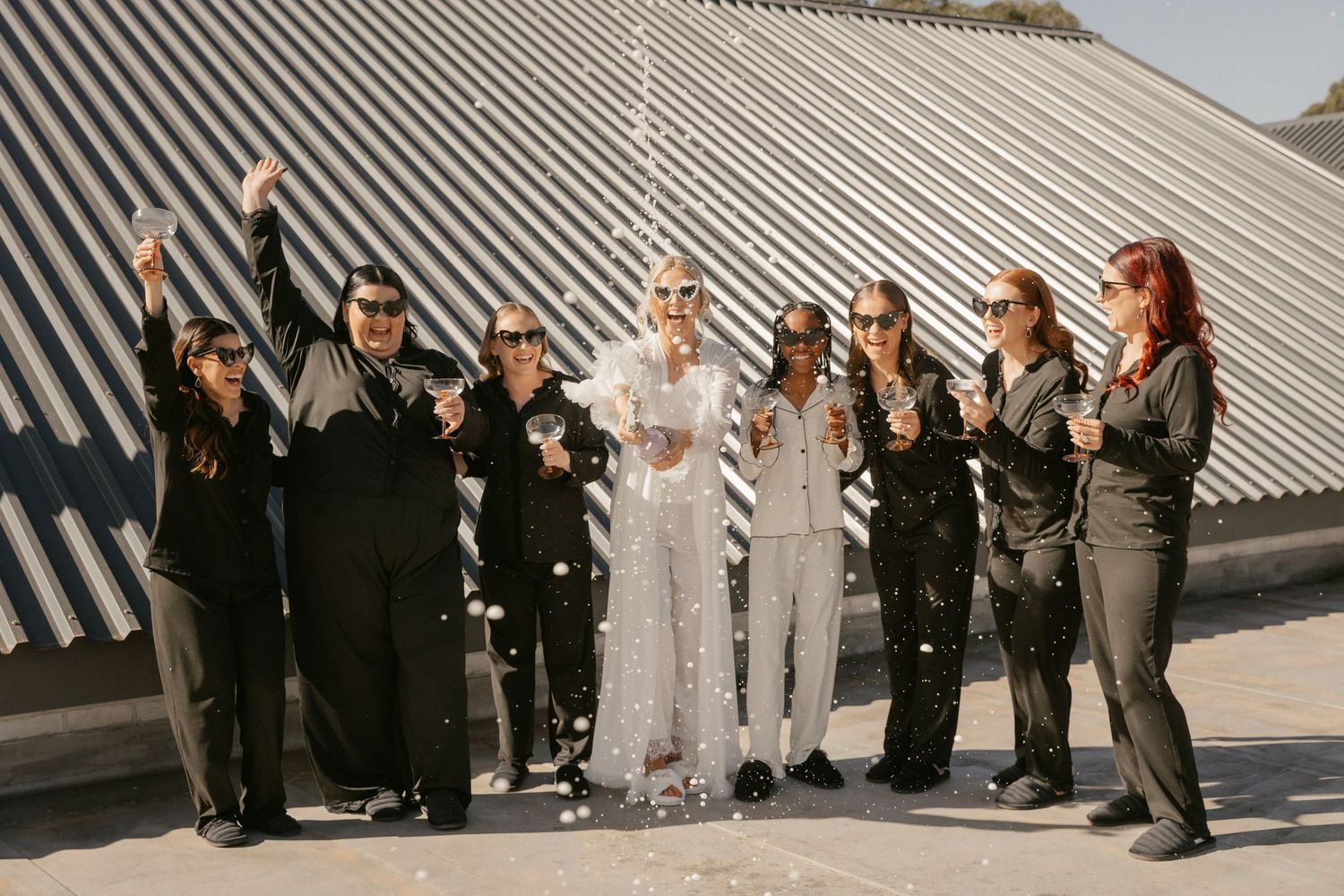 Wedding party celebrates with confetti outside modern building with diagonal striped architecture.