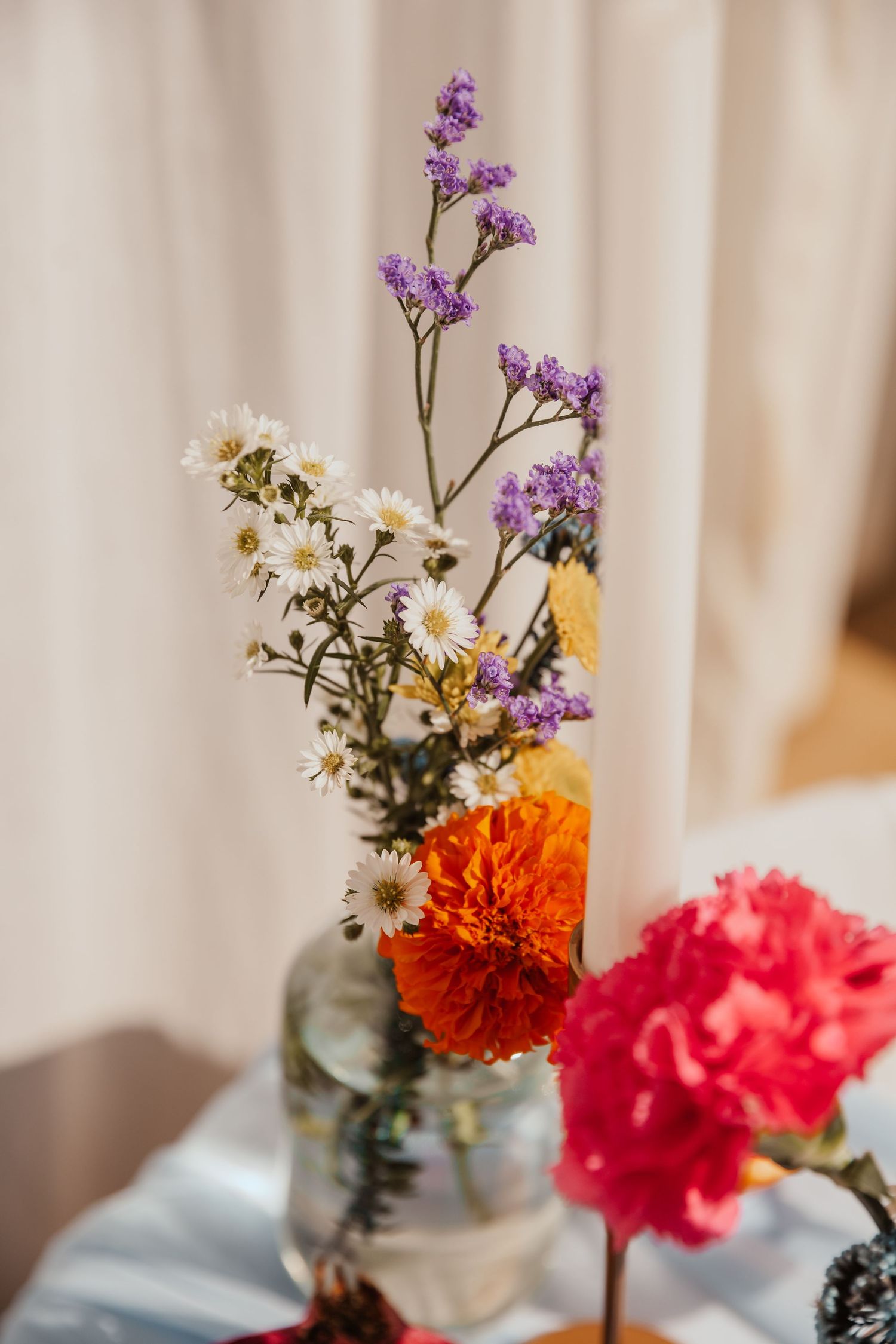 Close-up of mixed floral arrangement with daisies, carnations and purple flowers in glass vase.