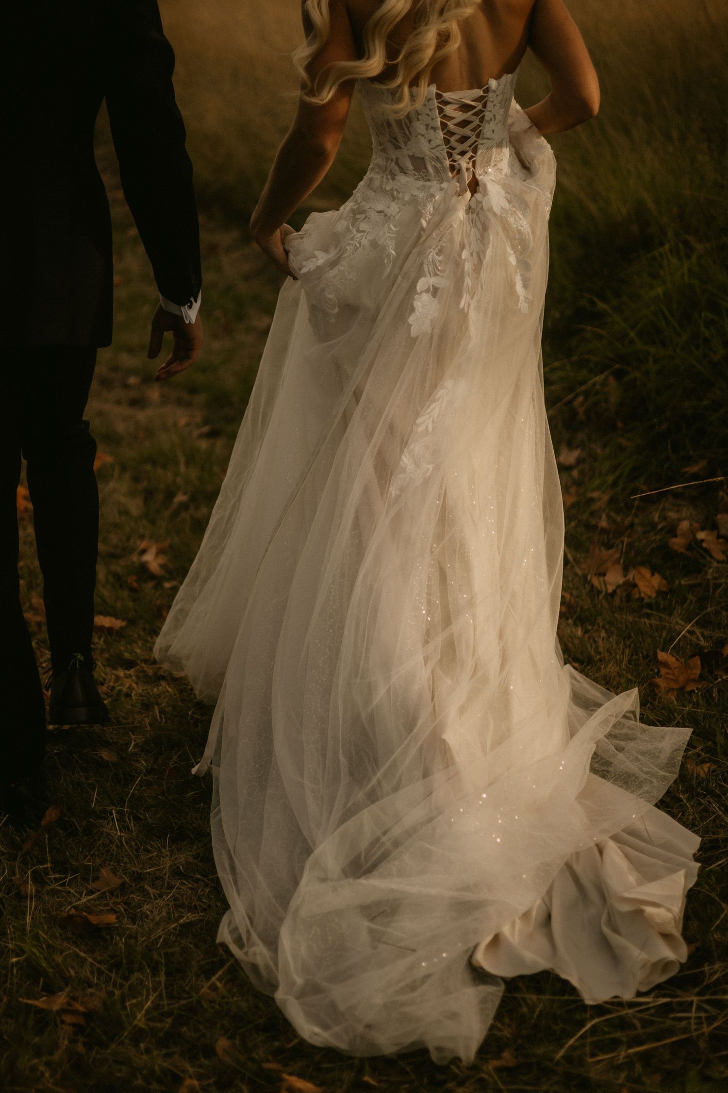 Elegant white wedding dress with corset back and flowing tulle train photographed outdoors at twilight.