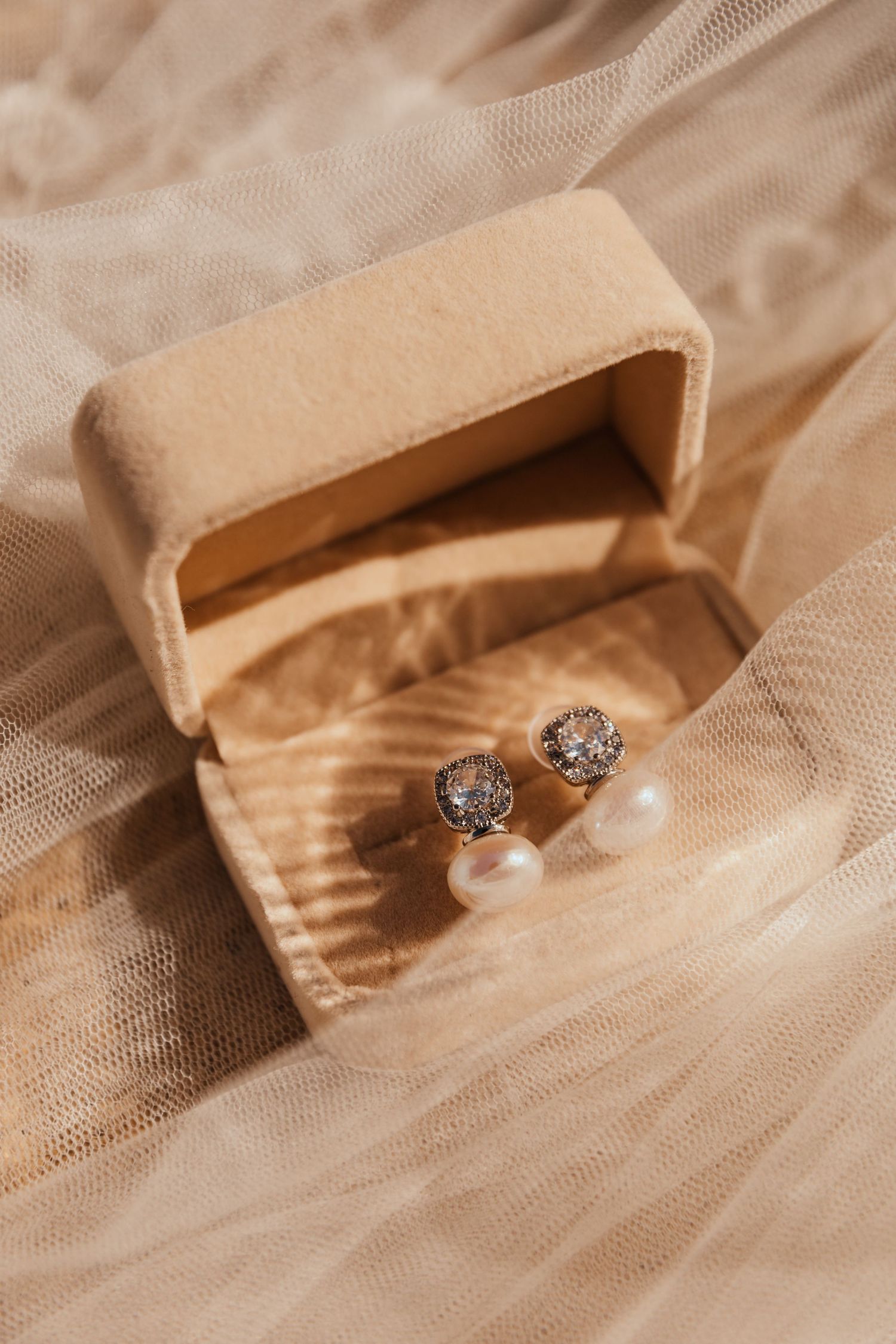 Elegant pearl and diamond stud earrings in beige velvet jewelry box.