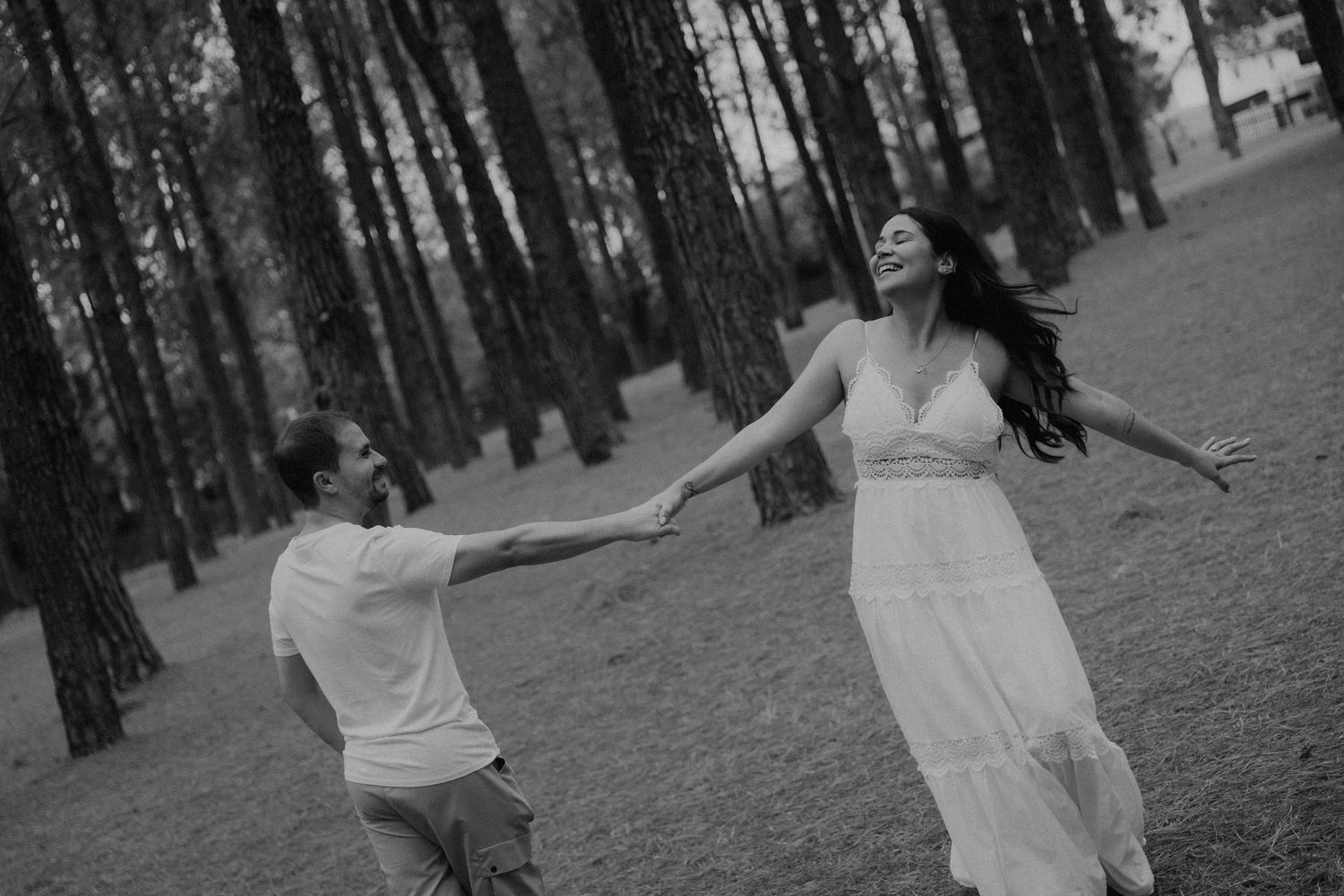 Person in white dress twirls joyfully through a serene pine forest on a sunny afternoon.