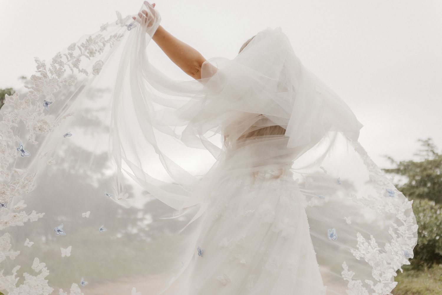 A flowing white wedding dress with delicate lace details hangs elegantly against a light background.