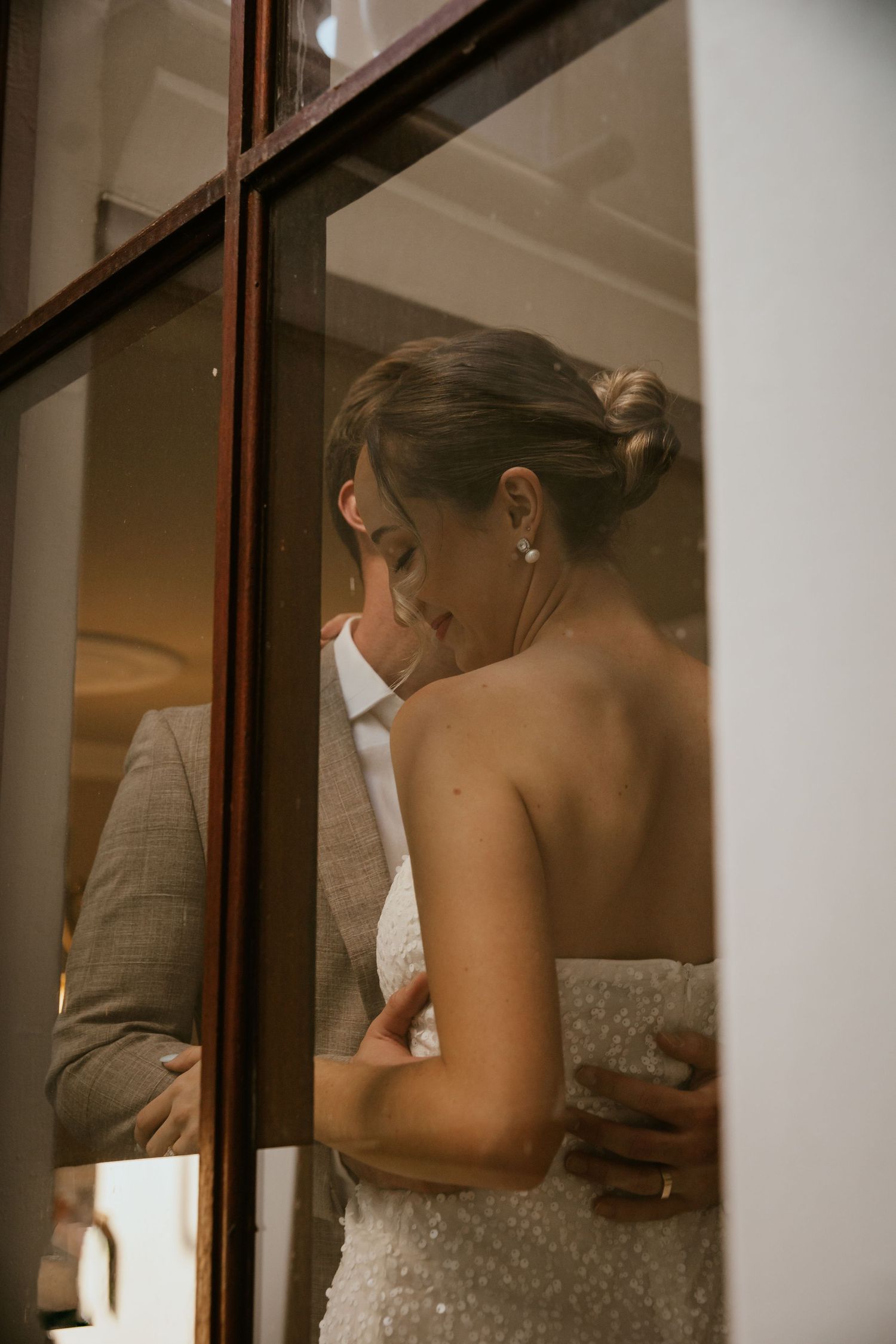 Wedding couple shares an intimate moment through a reflective window pane.