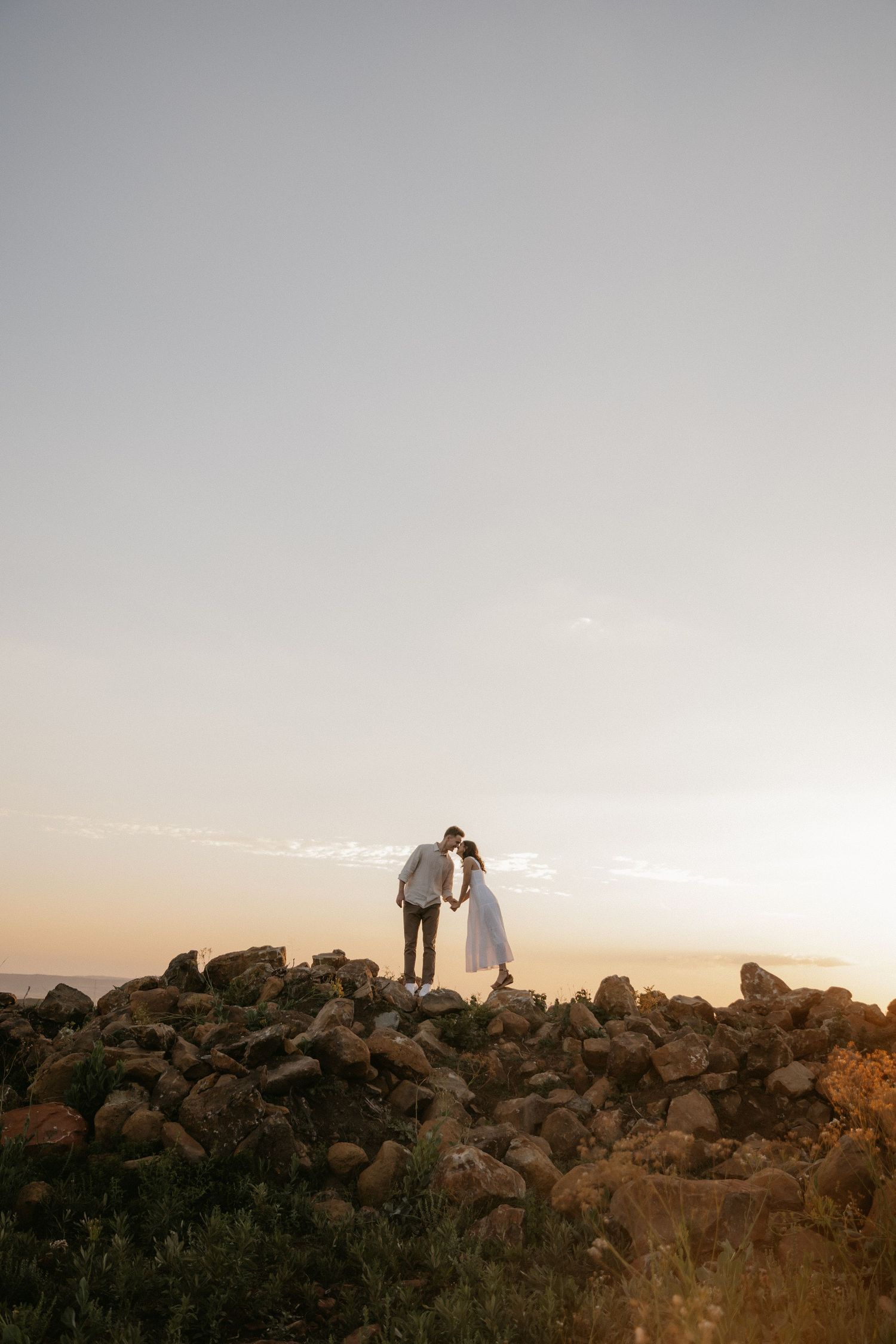 A silhouetted couple stands together on a rocky hill at sunset creating a romantic scenic moment.