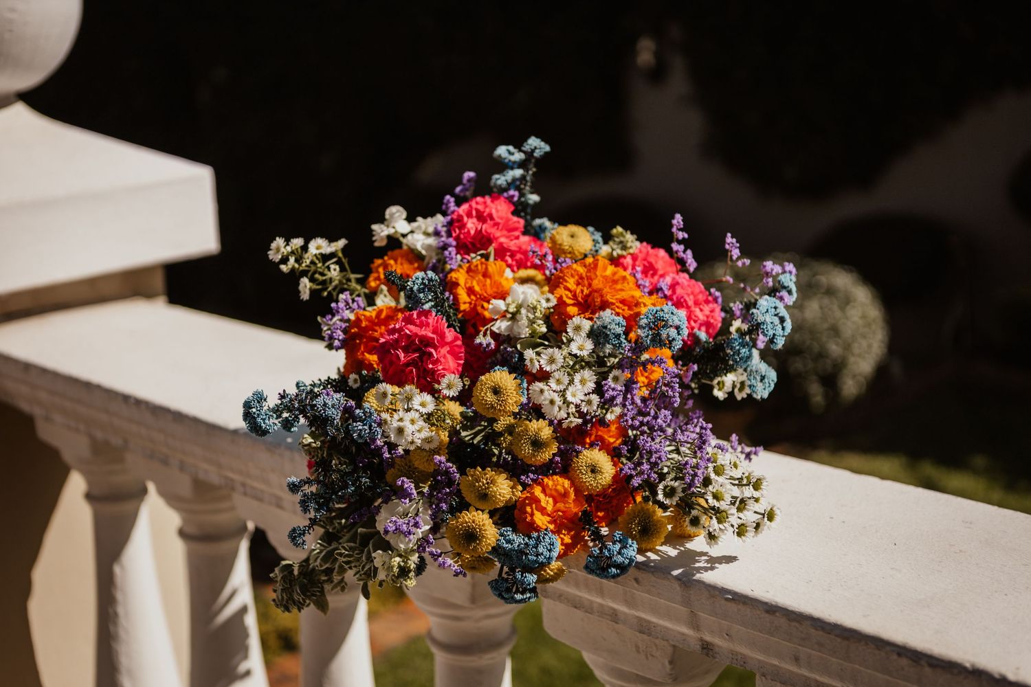 Vibrant wildflower bouquet with colorful blooms in sunlight on white railing.
