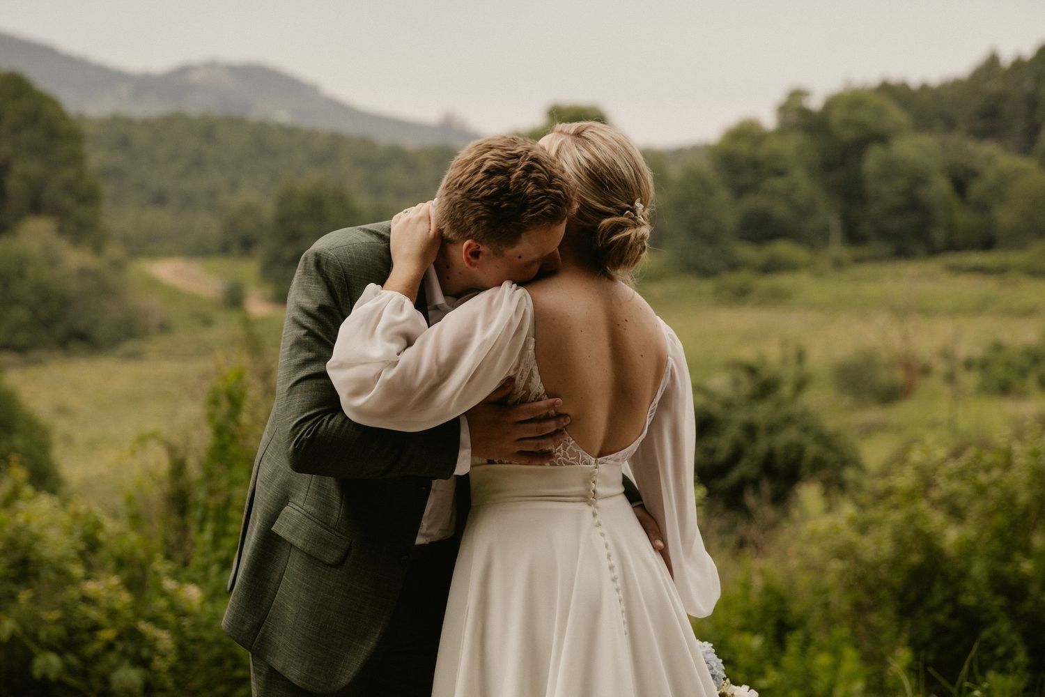A couple shares romantic moments in a scenic mountain landscape wearing wedding attire.