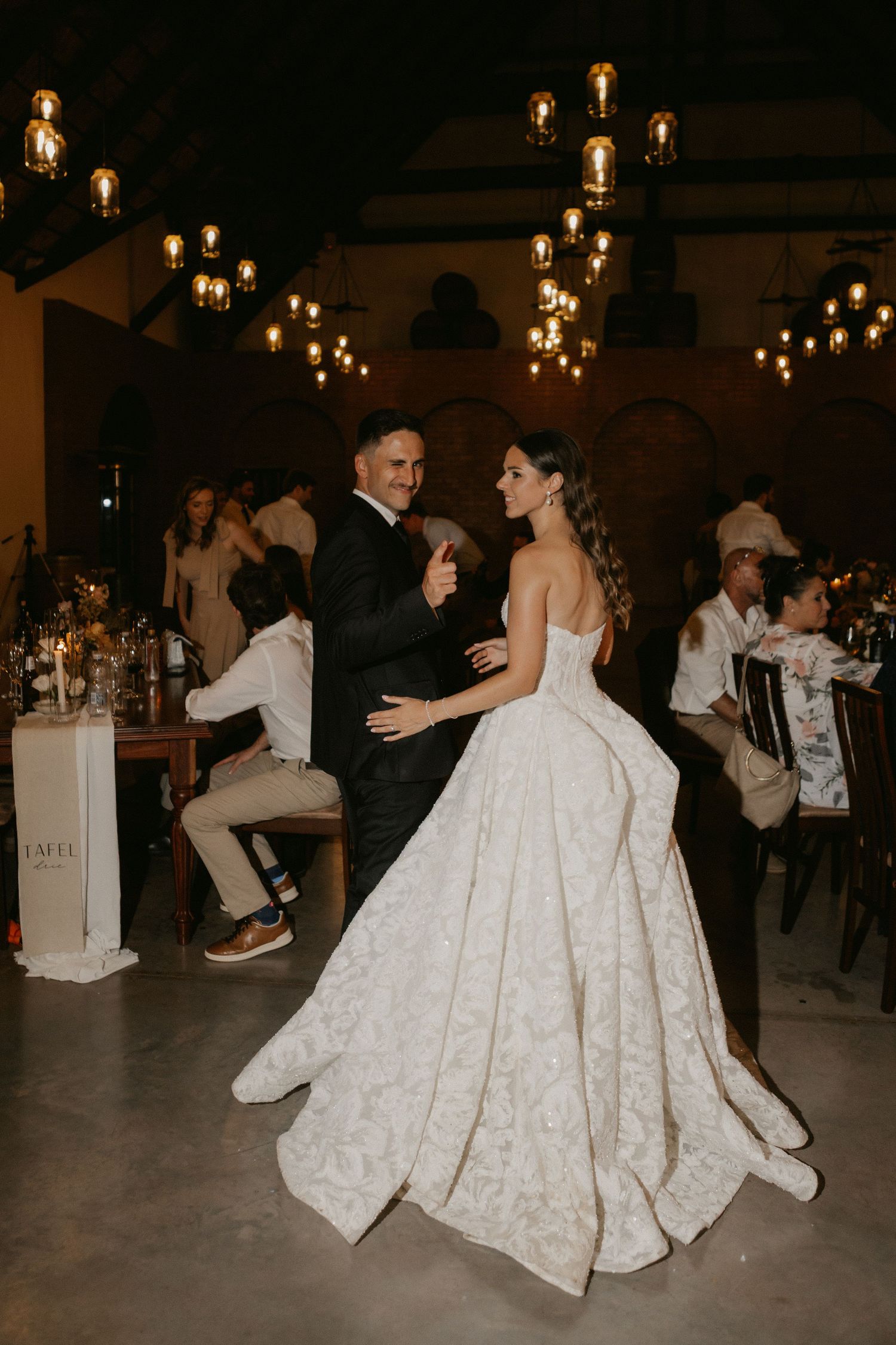 Bride and groom share first dance in elegant candlelit wedding venue with hanging Edison bulbs.