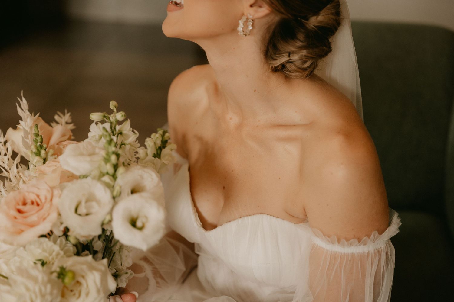 An elegant bride with a romantic off-shoulder white gown holds a delicate bouquet of blush and white florals.