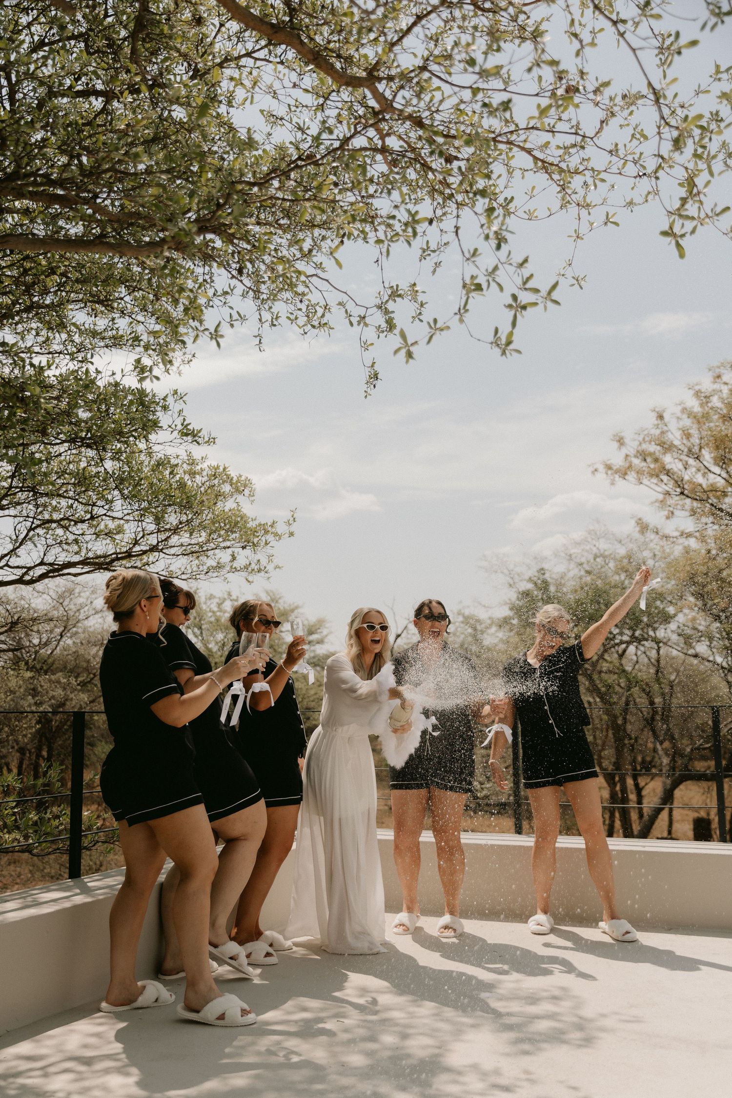 A fun wedding party poses playfully in sequence showing different dance moves on a bright sunny terrace.