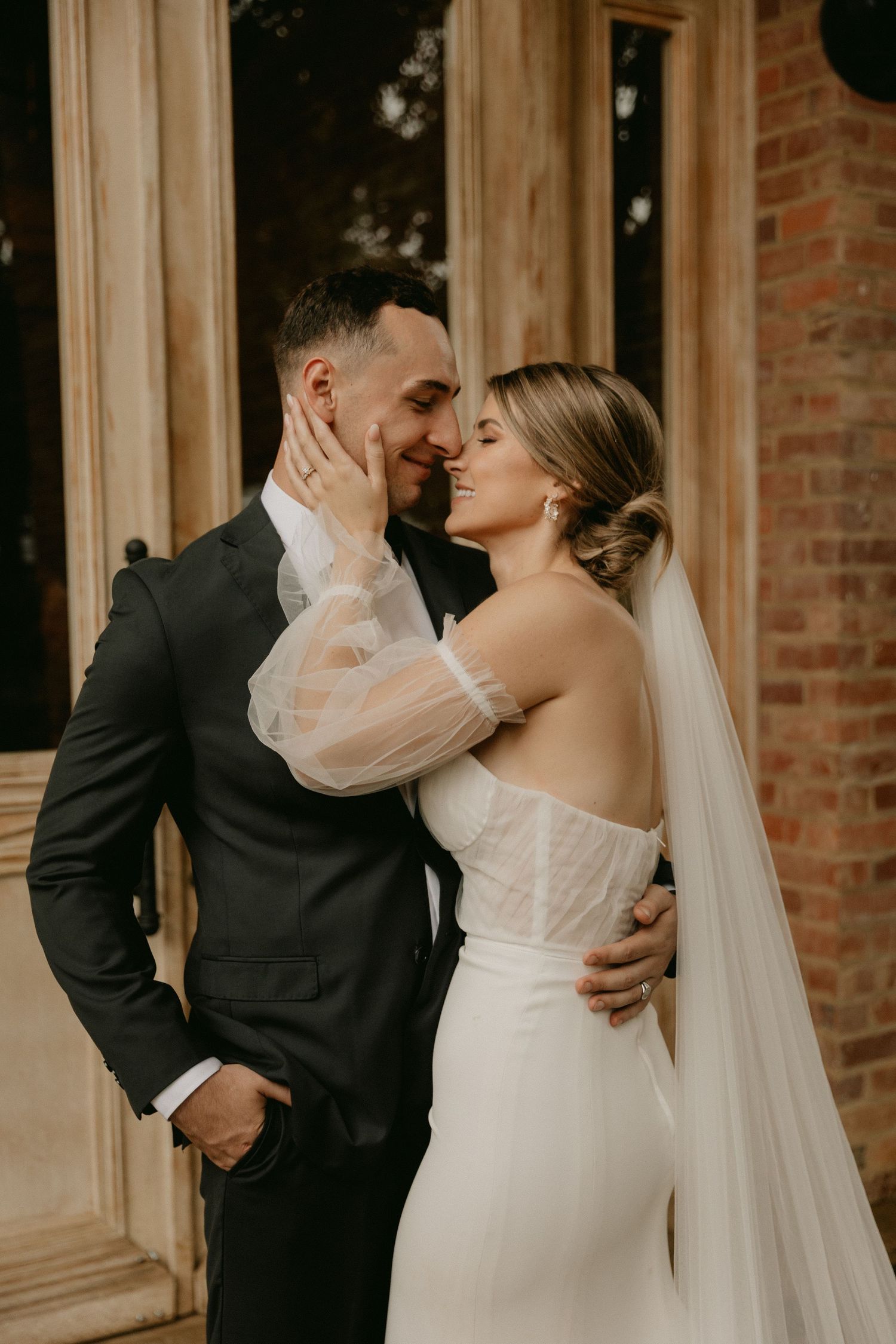 Intimate wedding moment captured as couple shares tender embrace in front of brick building during golden hour.