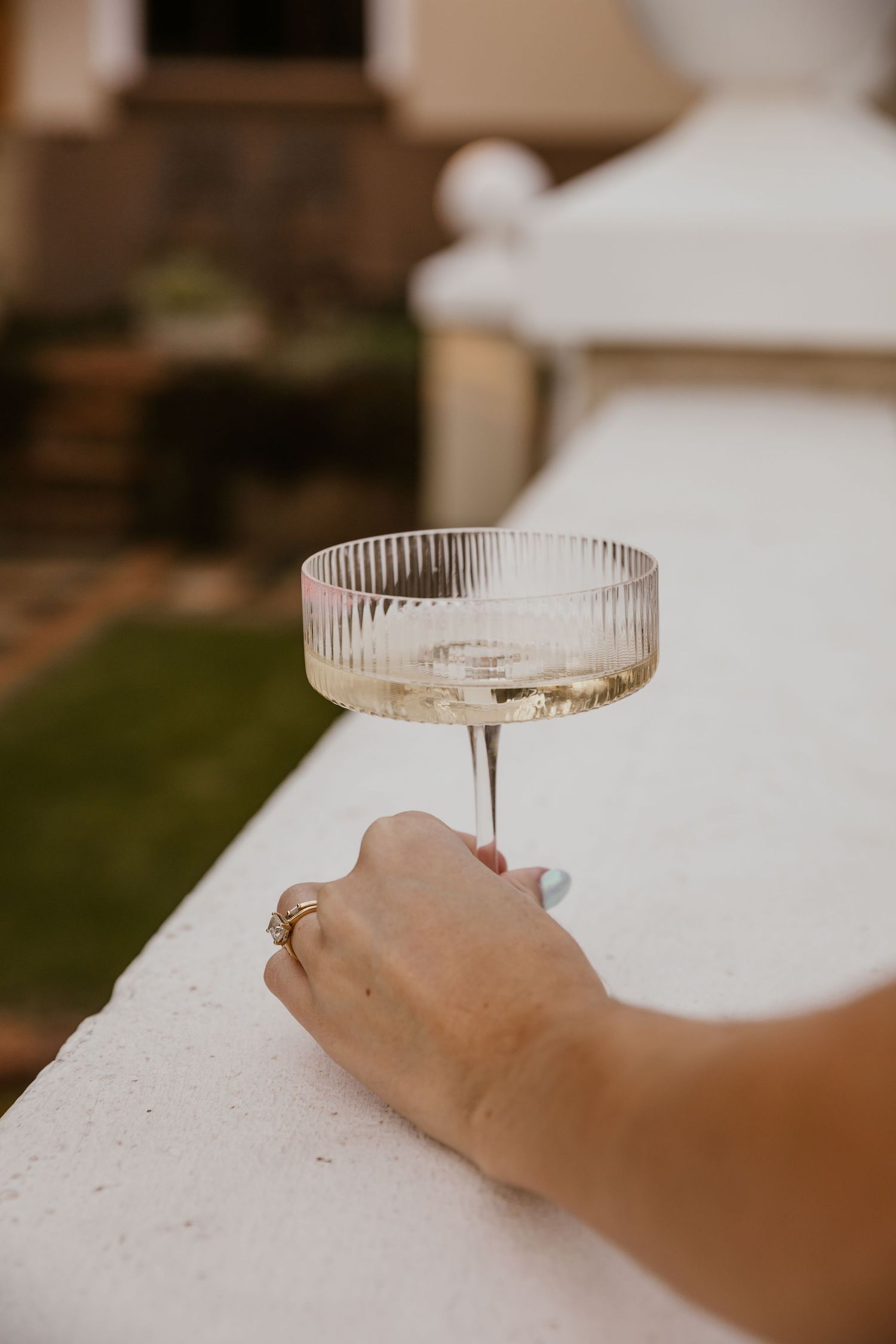 Hand holding a vintage champagne coupe glass on white surface during wedding celebration.