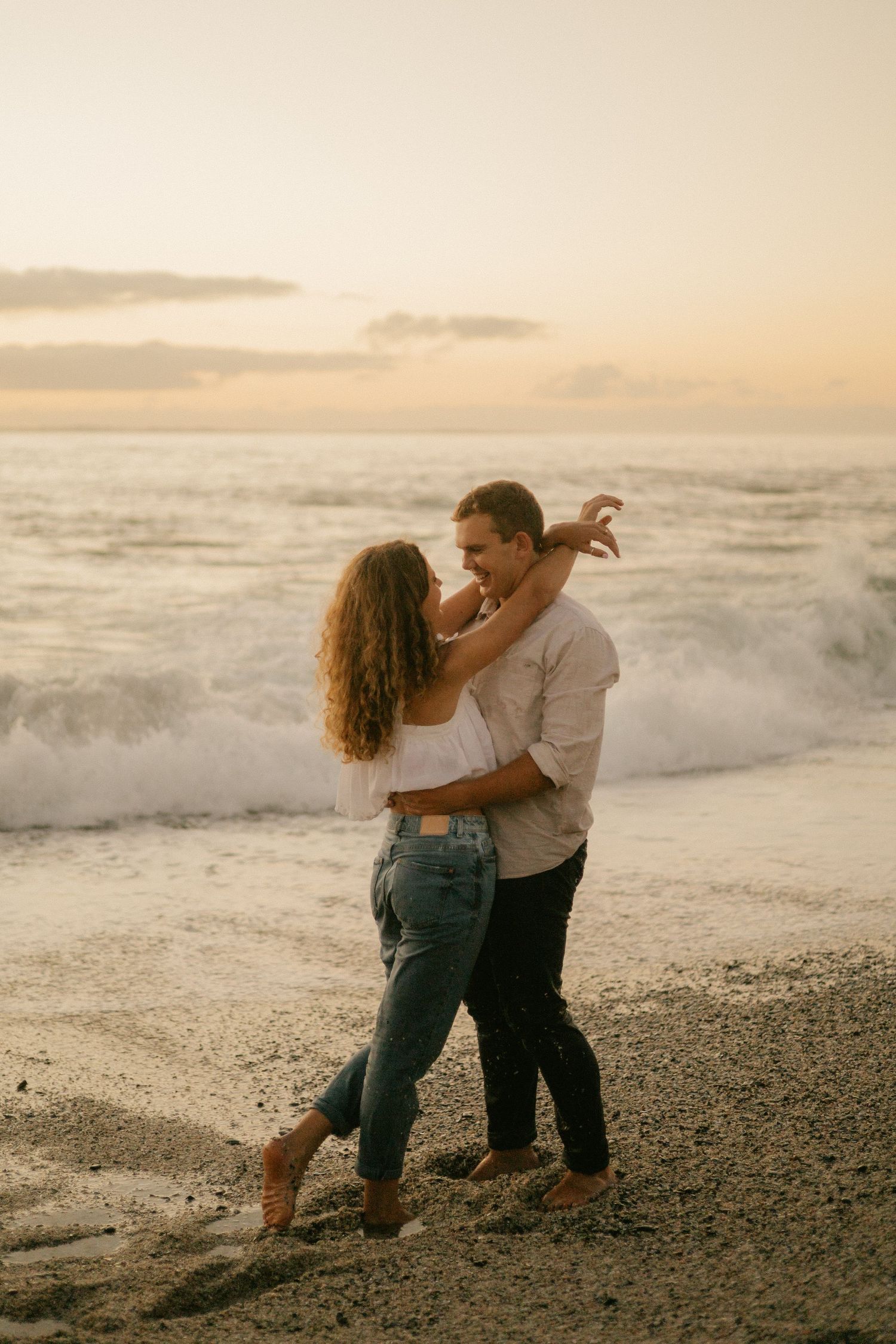 Romantic couple shares an intimate moment on the beach with crashing waves behind them.
