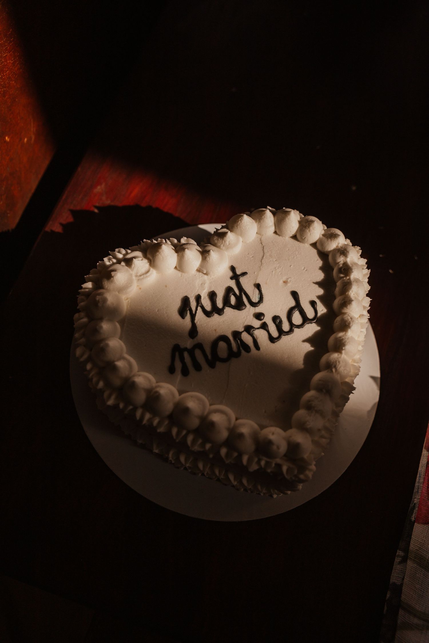 Heart-shaped wedding cake with 'just married' text in dark moody lighting.