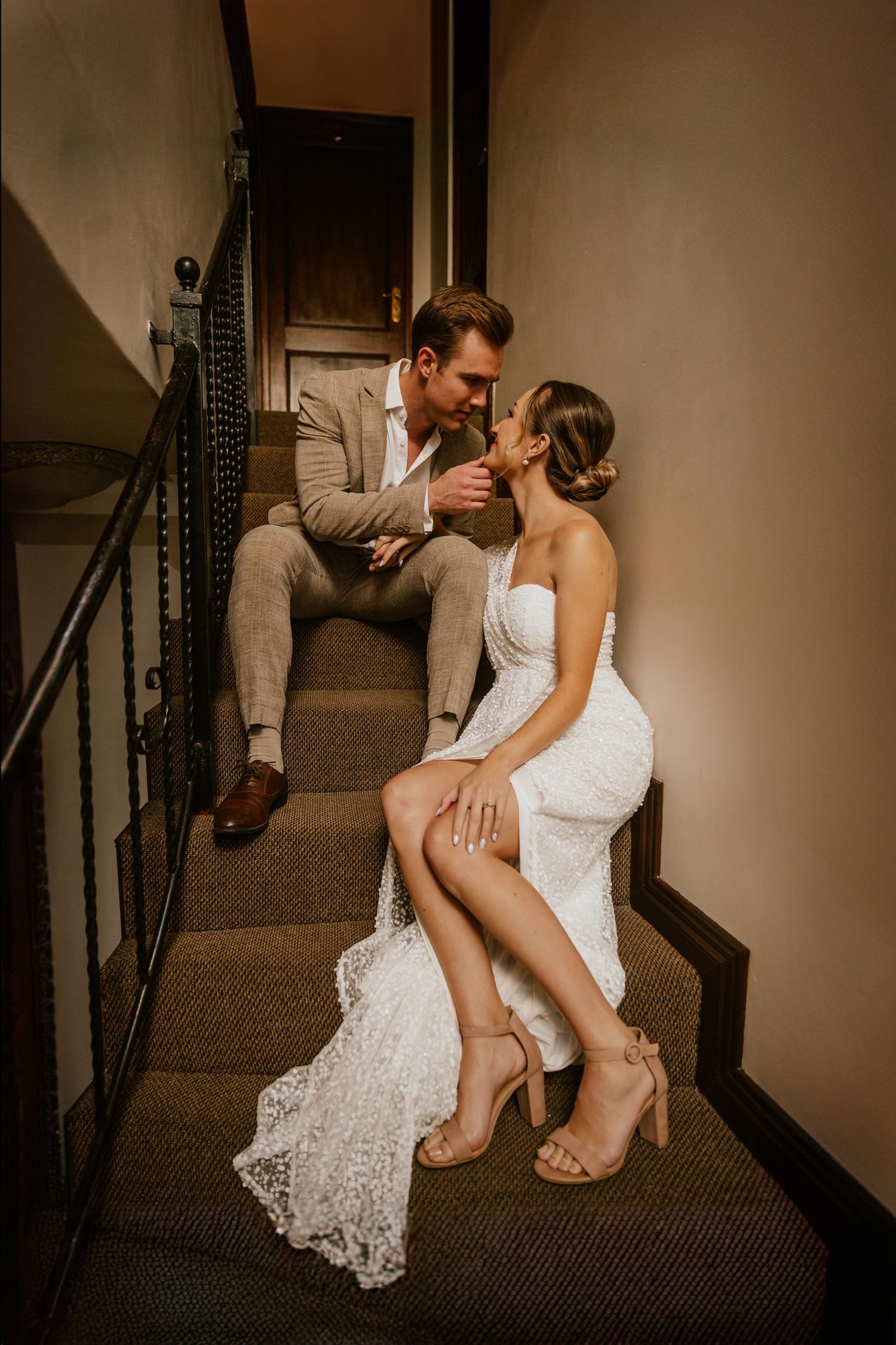 Romantic couple in wedding attire sharing an intimate moment on carpeted stairs.