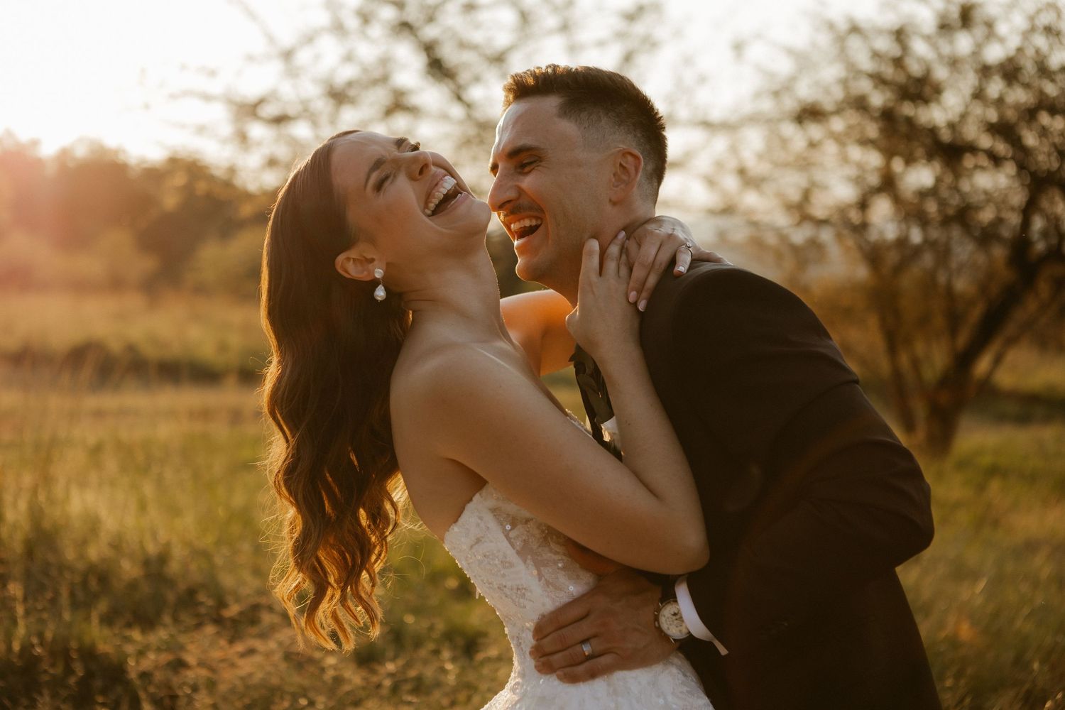 Joyful bride and groom embrace during golden hour outdoor wedding portrait.
