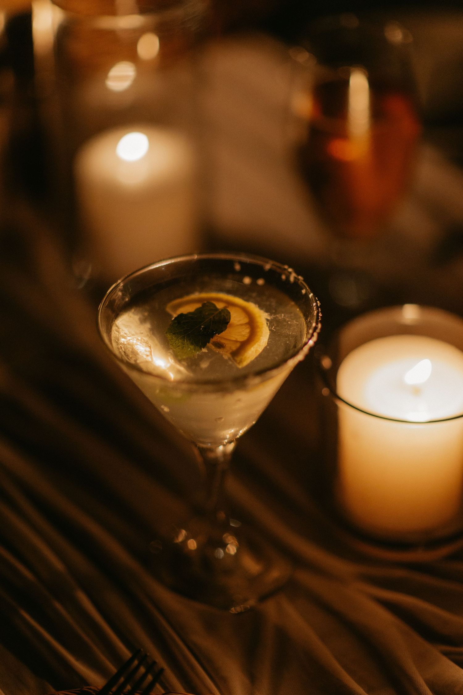 A series of martini glasses with lemon garnishes and candlelight creating a romantic ambiance at a dimly lit bar.