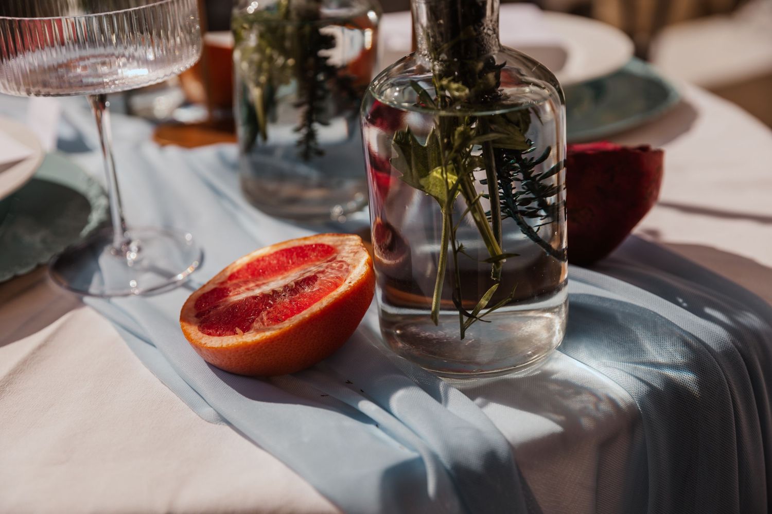 Table setting with fresh cut grapefruit, glass vase, and blue table runner.