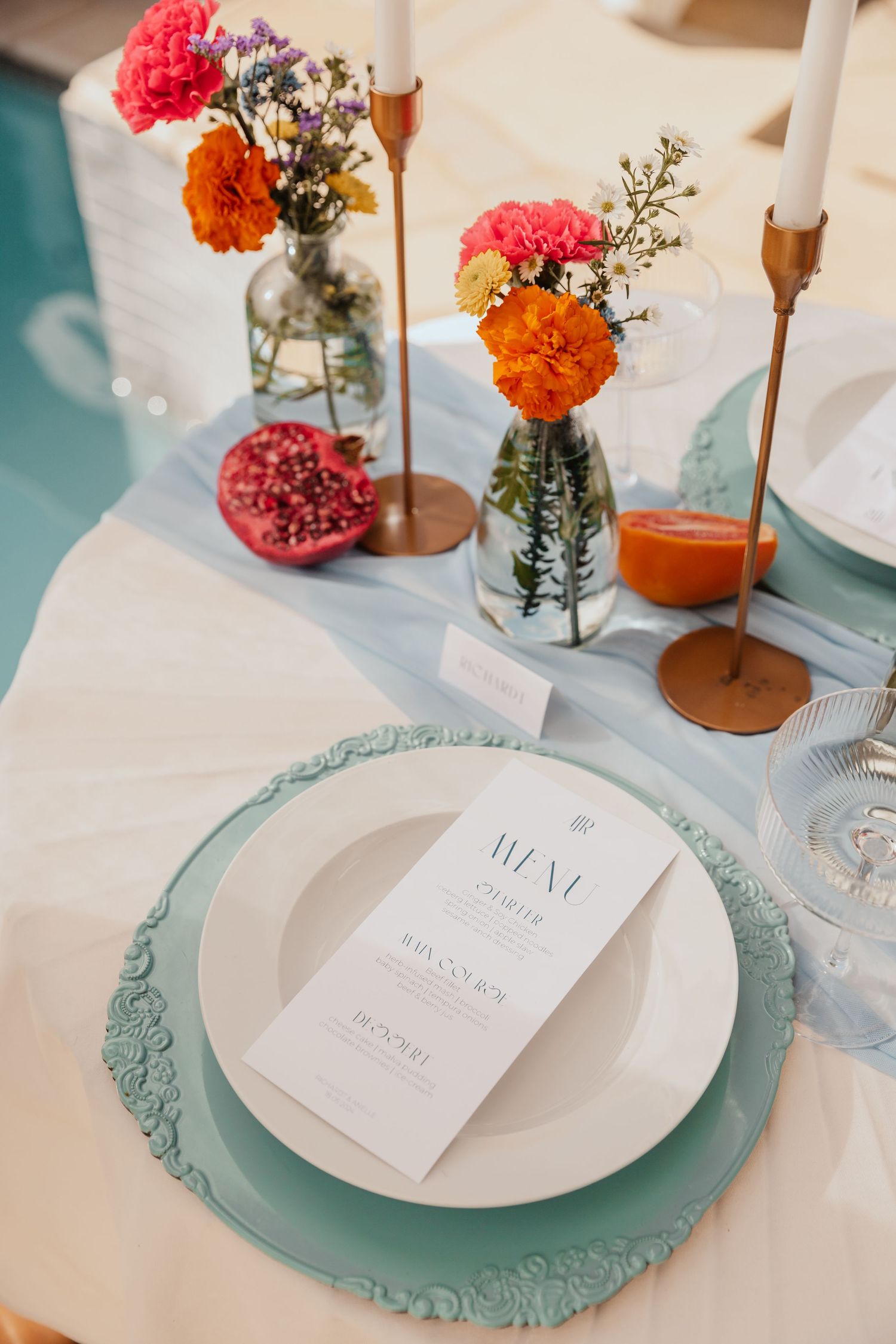 Elegant wedding table setting with coral flowers, turquoise charger plates, and gold candlesticks.