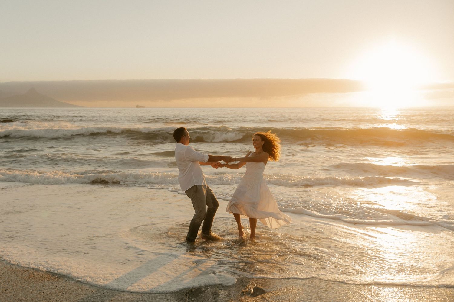 A couple dances together in the ocean waves during a golden sunset.