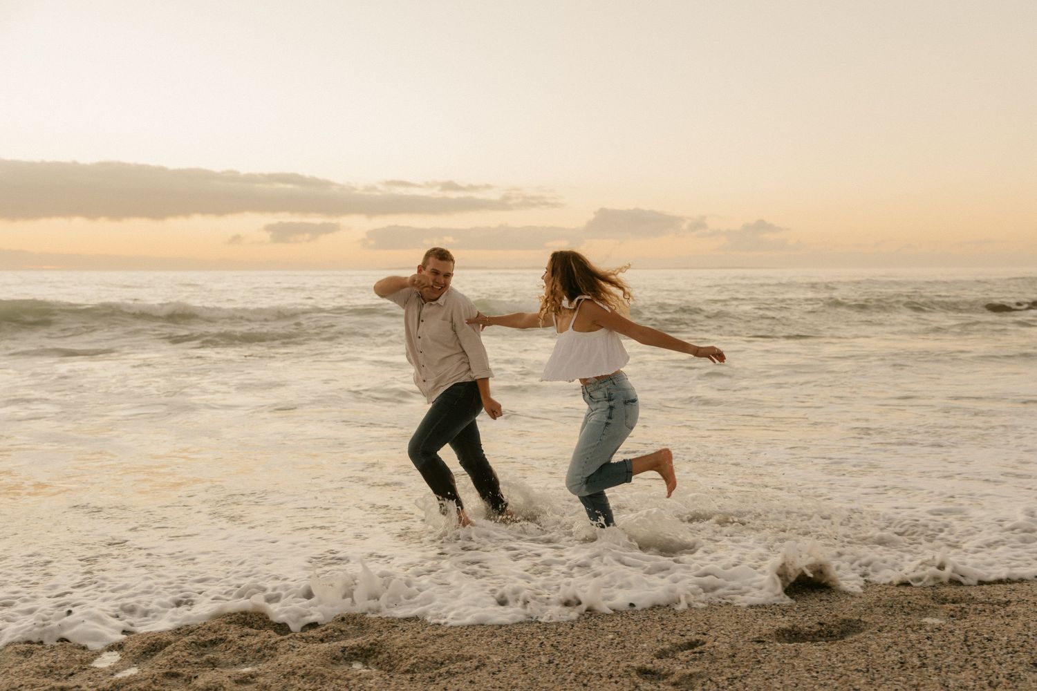 Two joyful people leap in the air together on a beachfront at sunset.