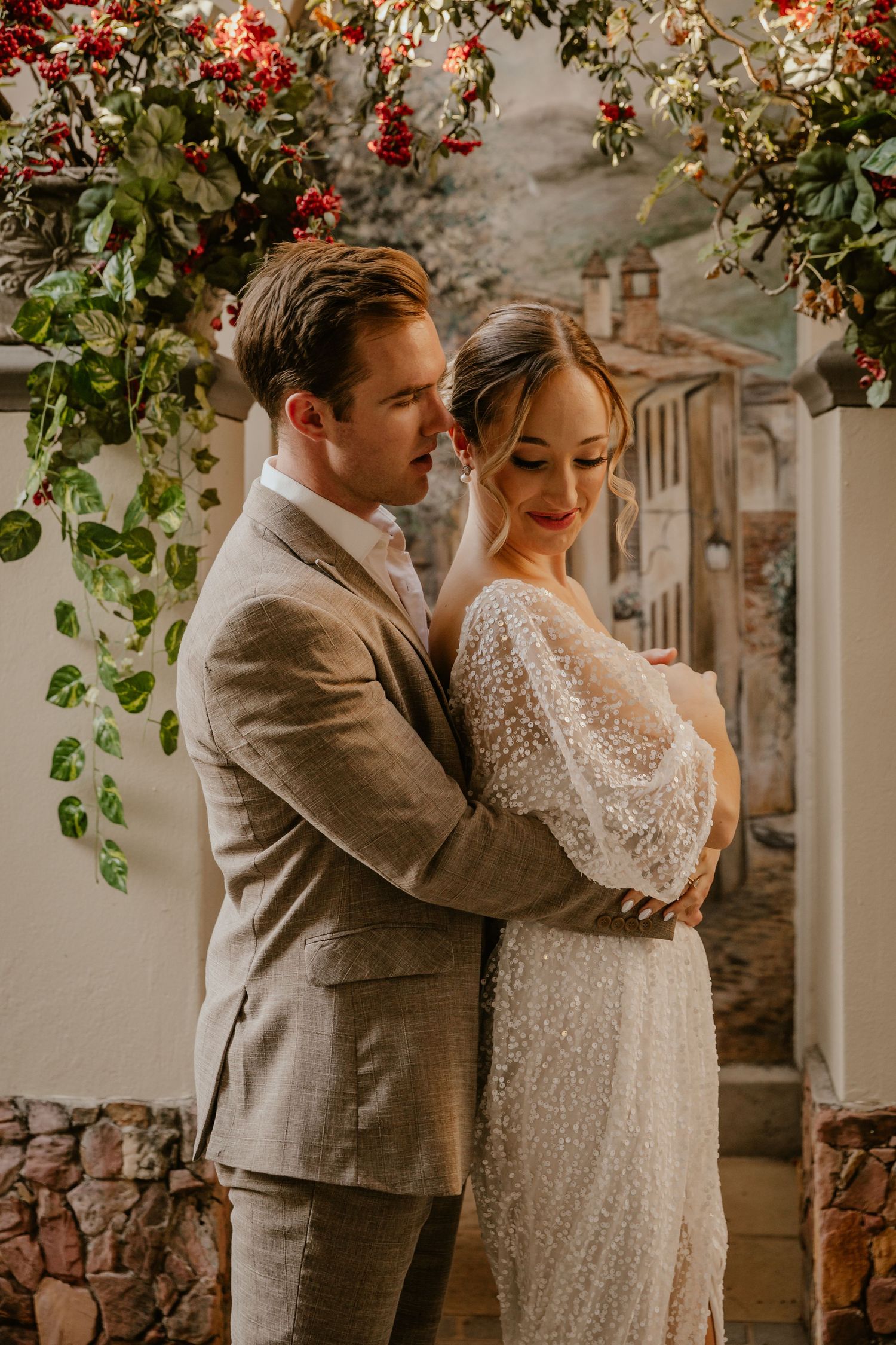 Romantic couple portrait under flowering arbor with Mediterranean architecture.