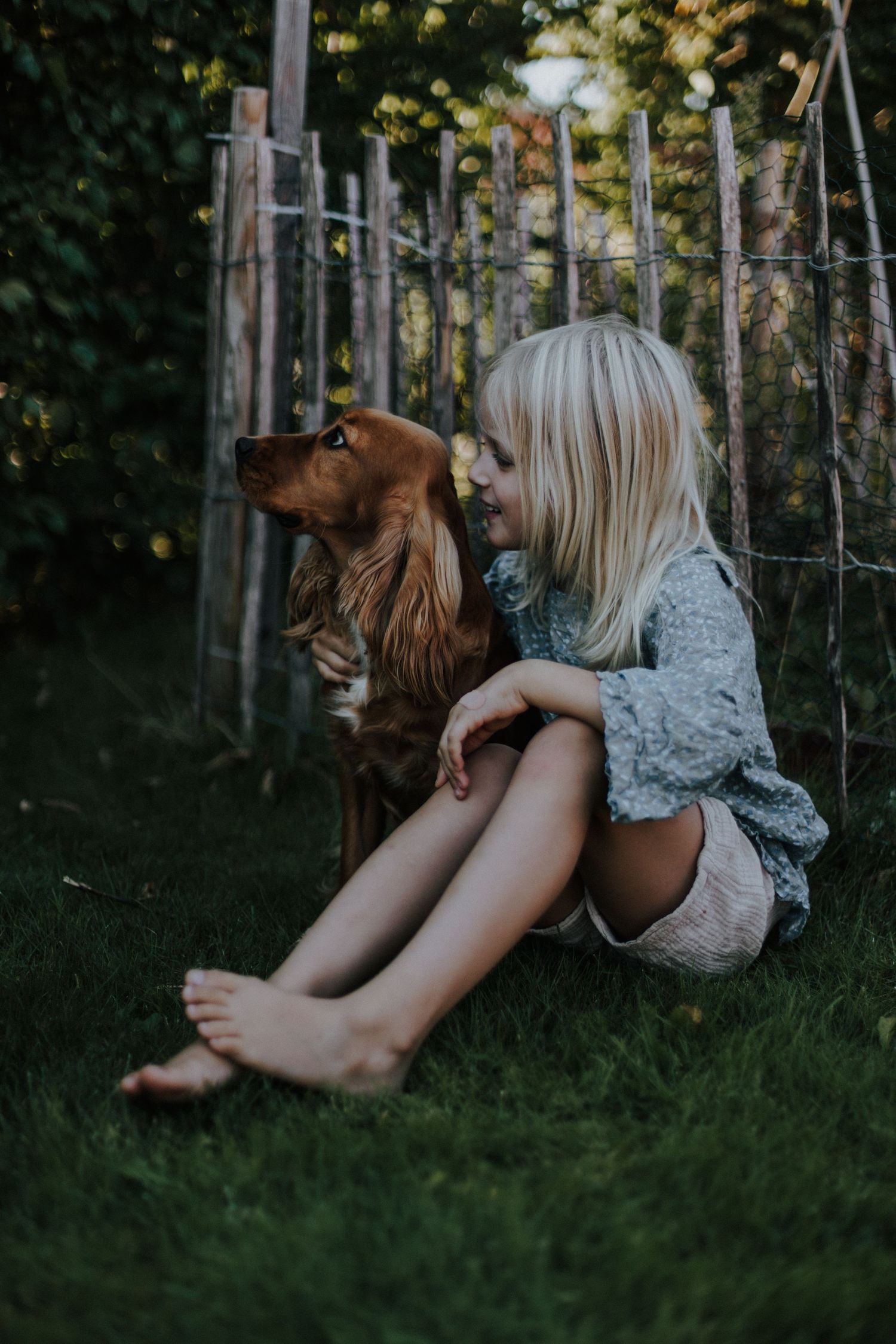 Närbild i mjukt ljus på ett sittande barn i en kärleksfull och avslappnat stund i trädgården med sin hund. Porträttfotografering i Varnum.