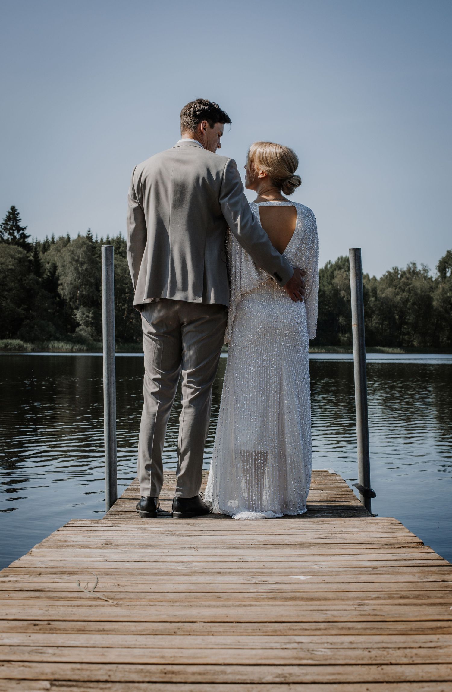 Par som håller om varandra på en brygga vid en lugn sjö i romantisk bröllopsfotografering i Varnum.