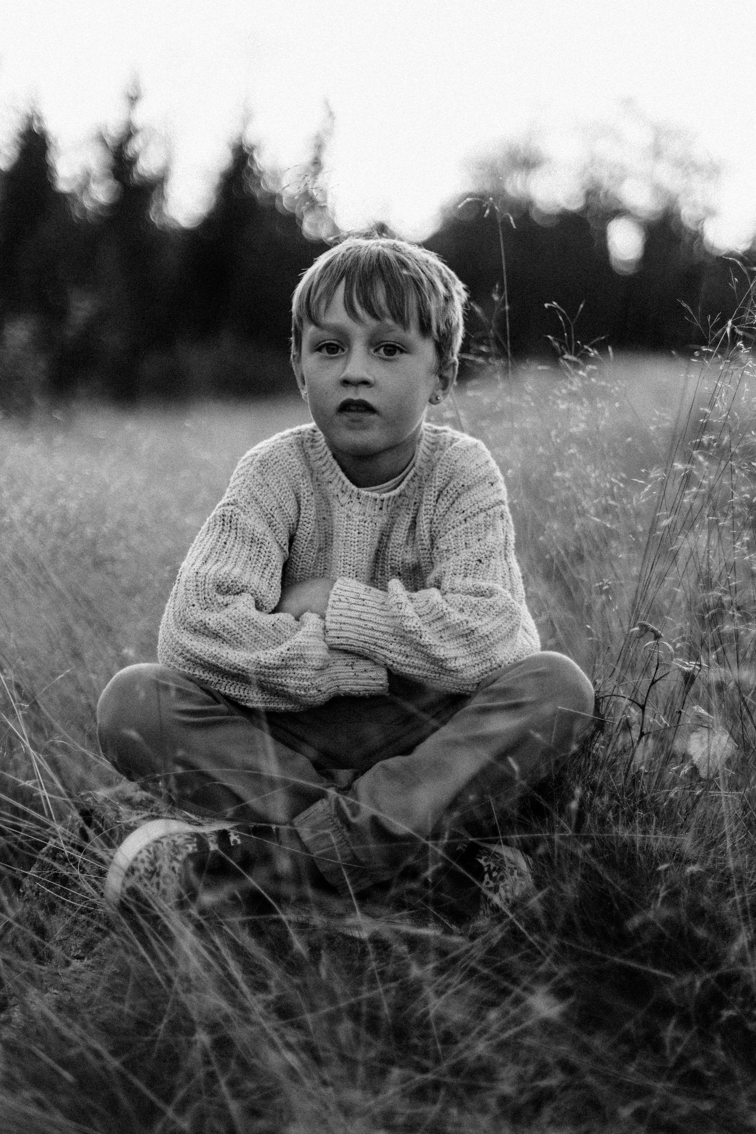 Svartvitt porträtt av ett barn som sitter i naturen i mjukt ljus. Porträttfotografering i Västra Götaland.
