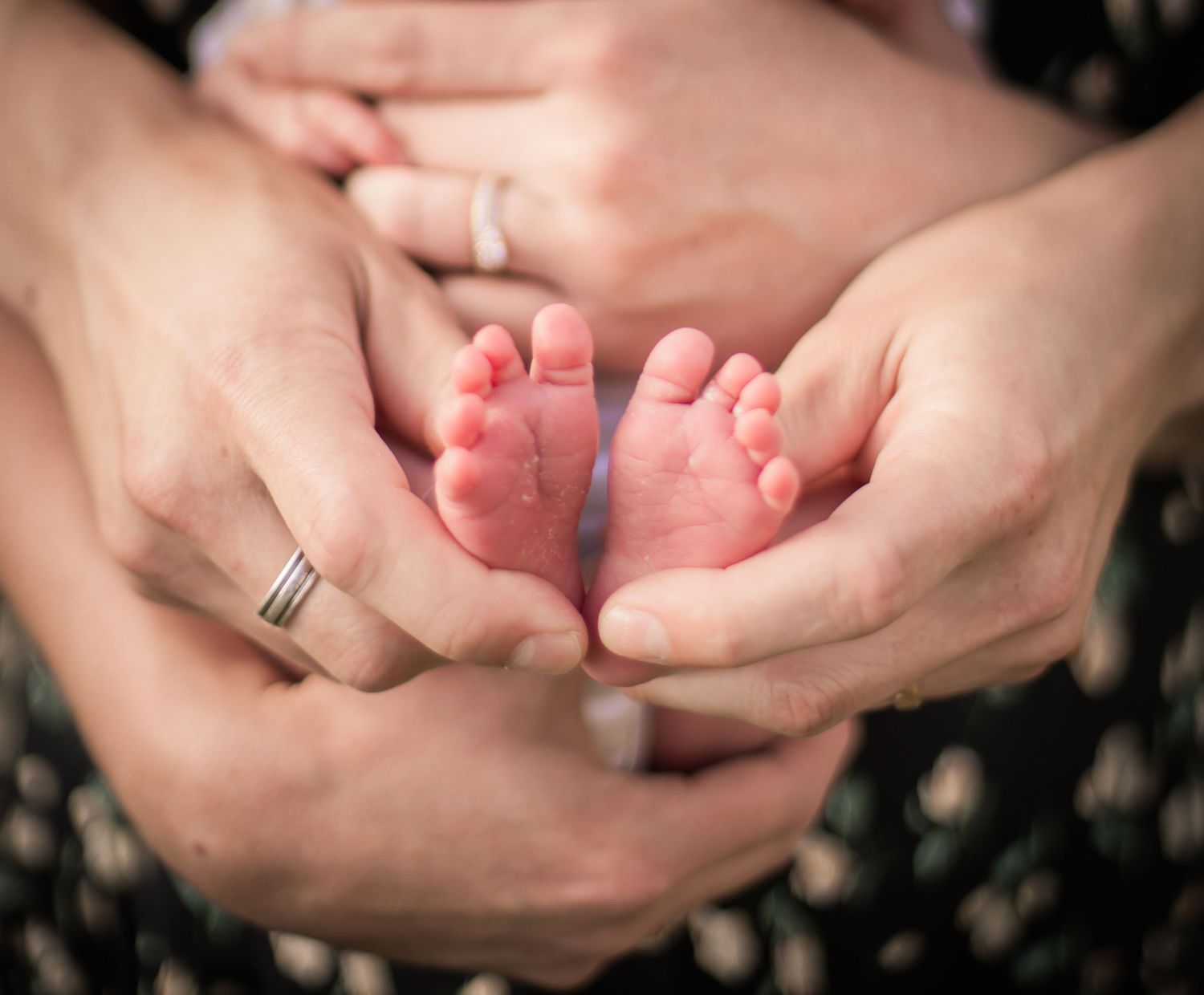 Närbild på nyfödda fötter i föräldrars händer i en varm och naturligt familjefotografering.