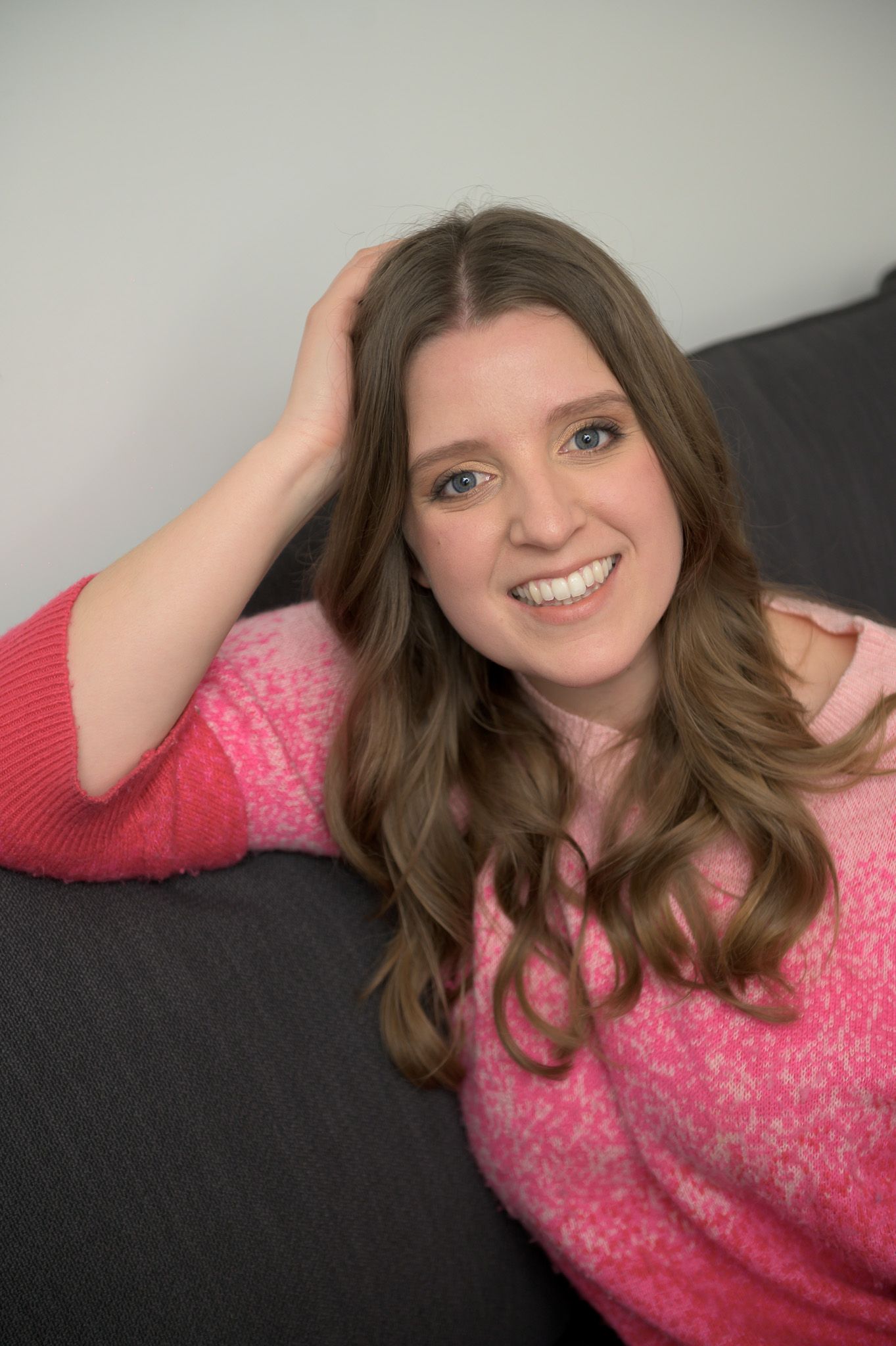 Relaxed portrait on gray couch wearing pink patterned sweater.
