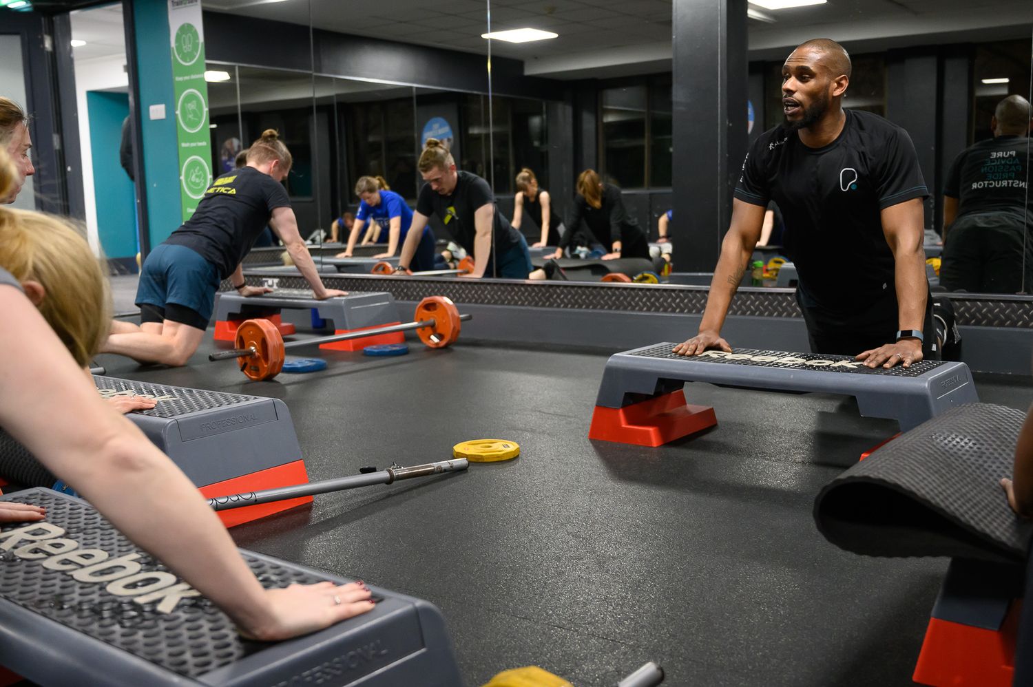 Group fitness class with people using step platforms and weights in modern gym setting.