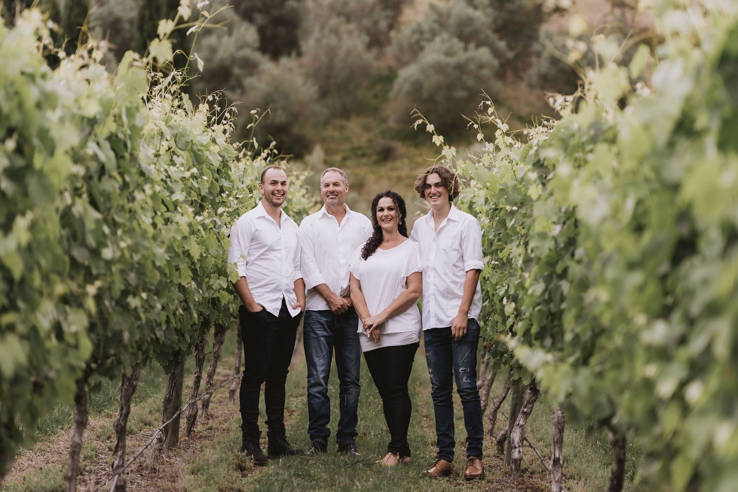 A group stands together between rows of grape vines in a scenic vineyard setting during a sunny day.