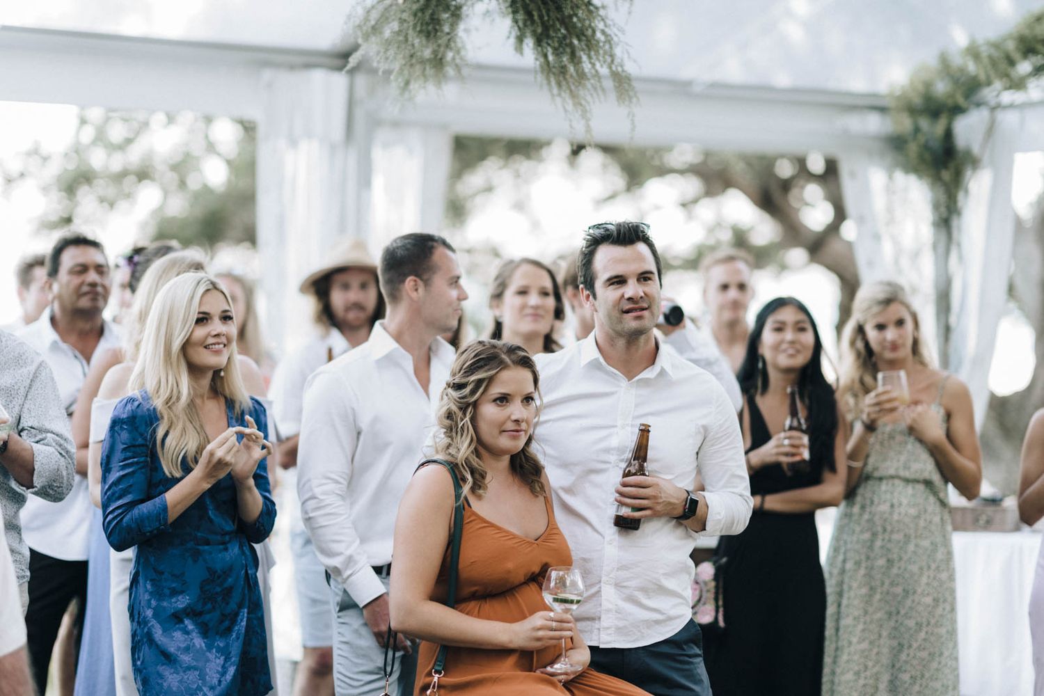 Wedding guests gathered under a white tent enjoying drinks and celebrating at an outdoor reception.